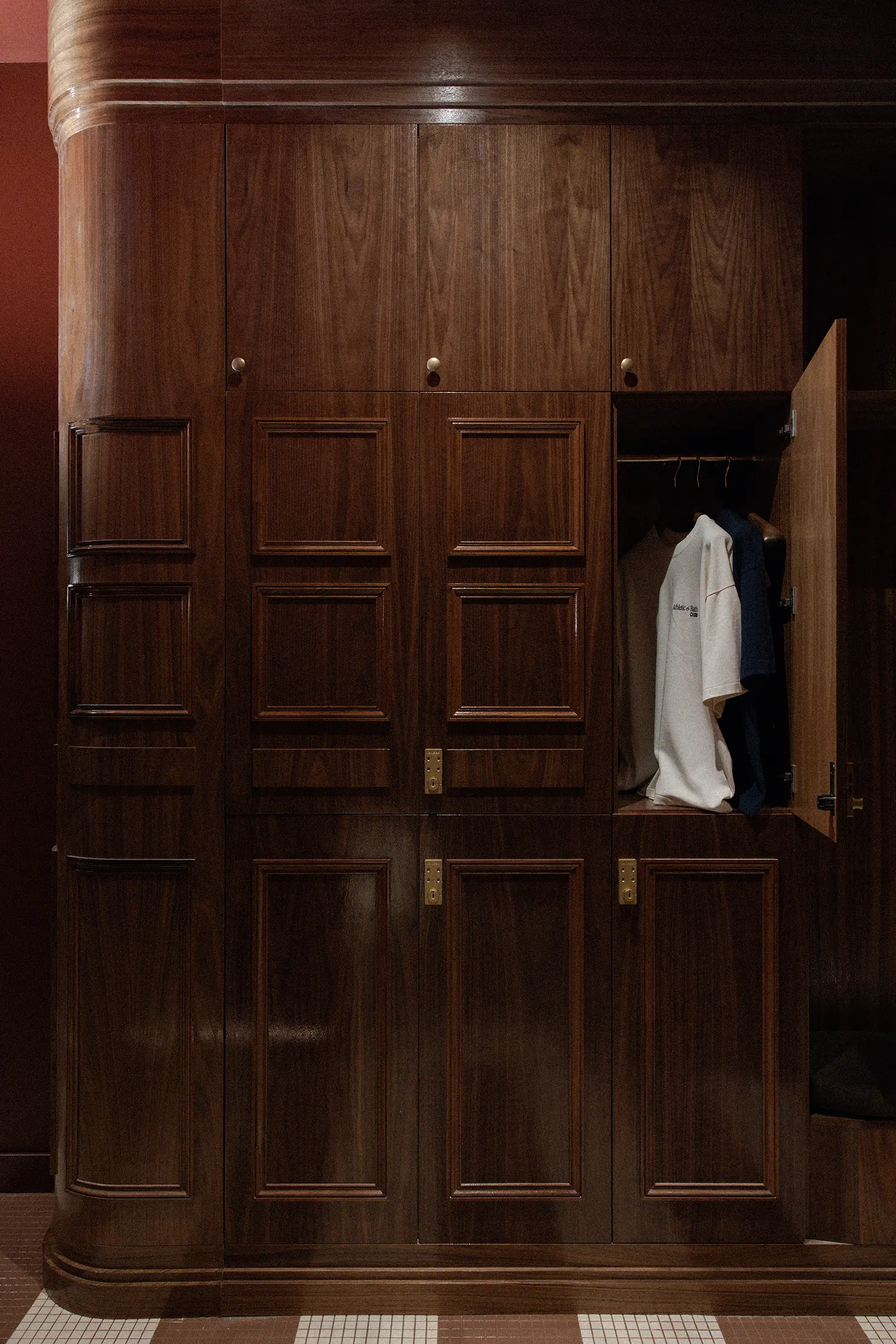 Tall, custom-made American walnut lockers with traditional molding and brass hardware in a dark locker room.