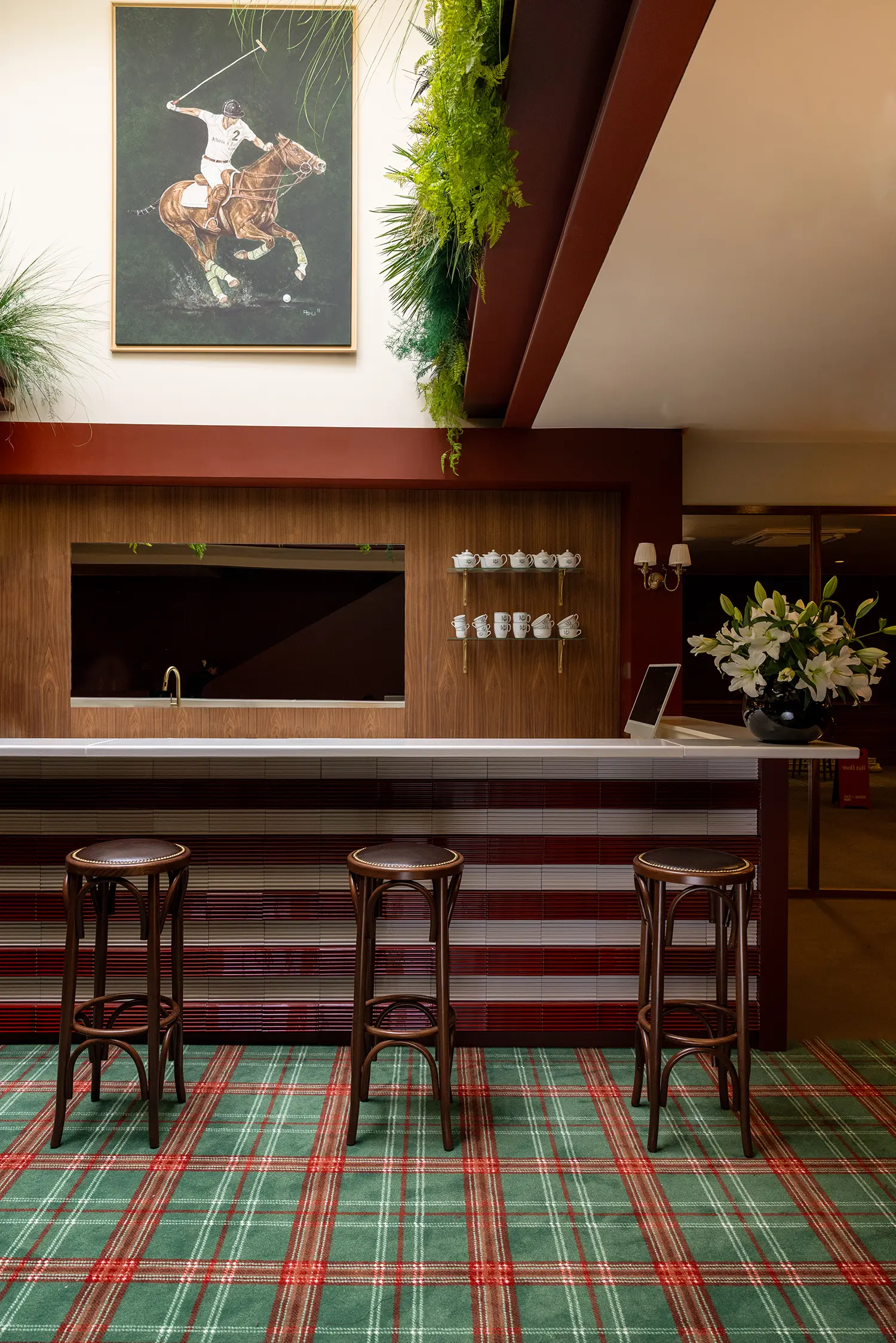 A bar area with a white countertop, striped tile base, green tartan carpet, and a polo-themed painting above.