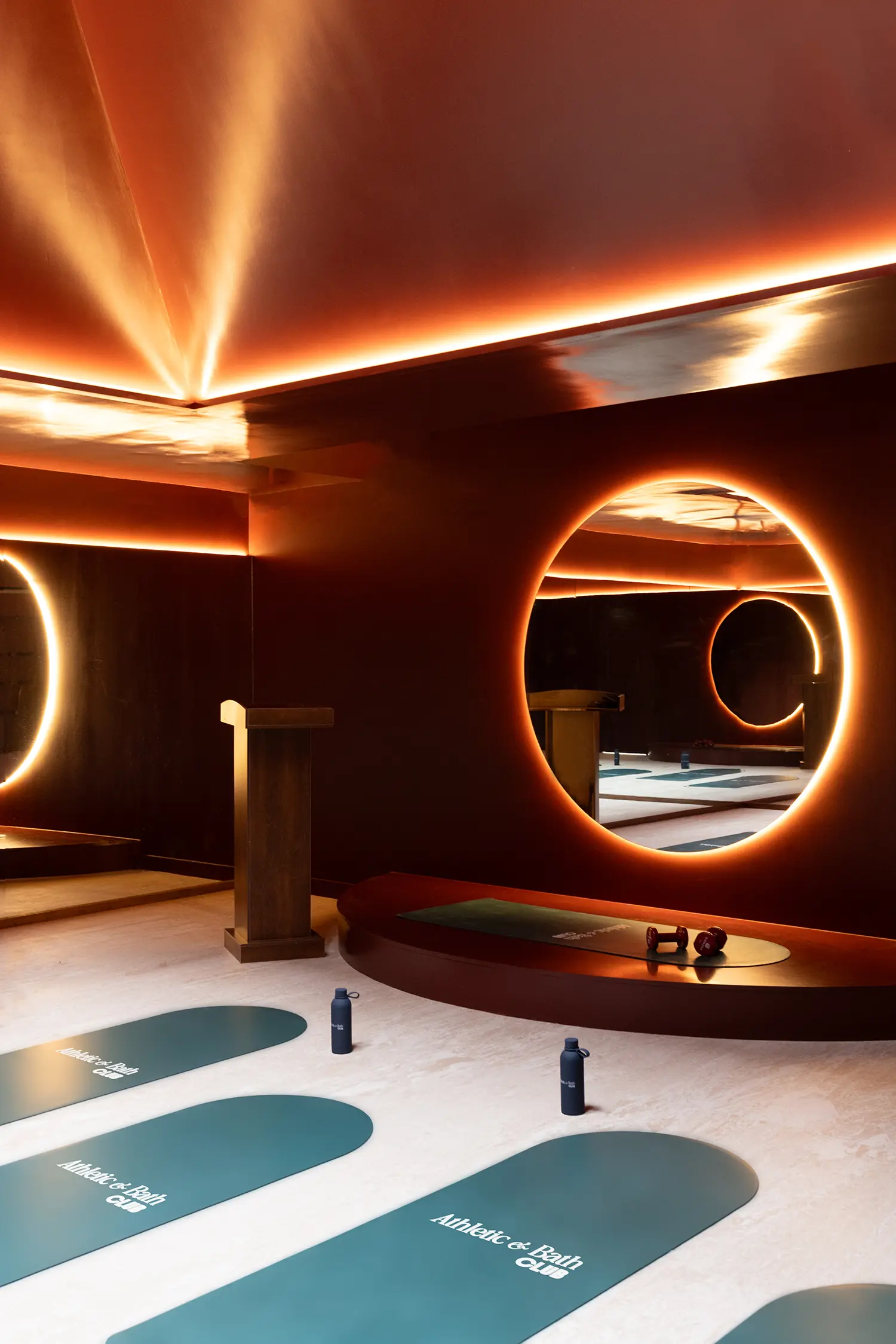 A dark fitness studio with glowing circular mirrors, turquoise yoga mats, and a wood podium.