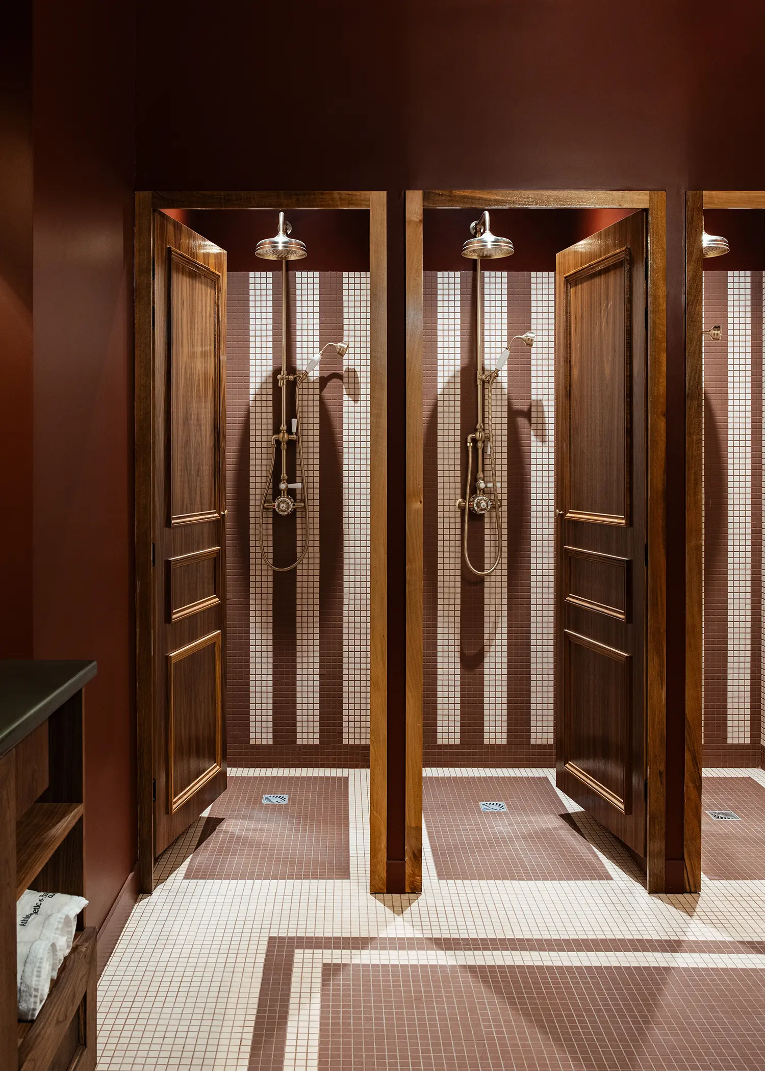 Private shower stalls with American walnut doors and geometric mosaic tile patterns in white and brown.