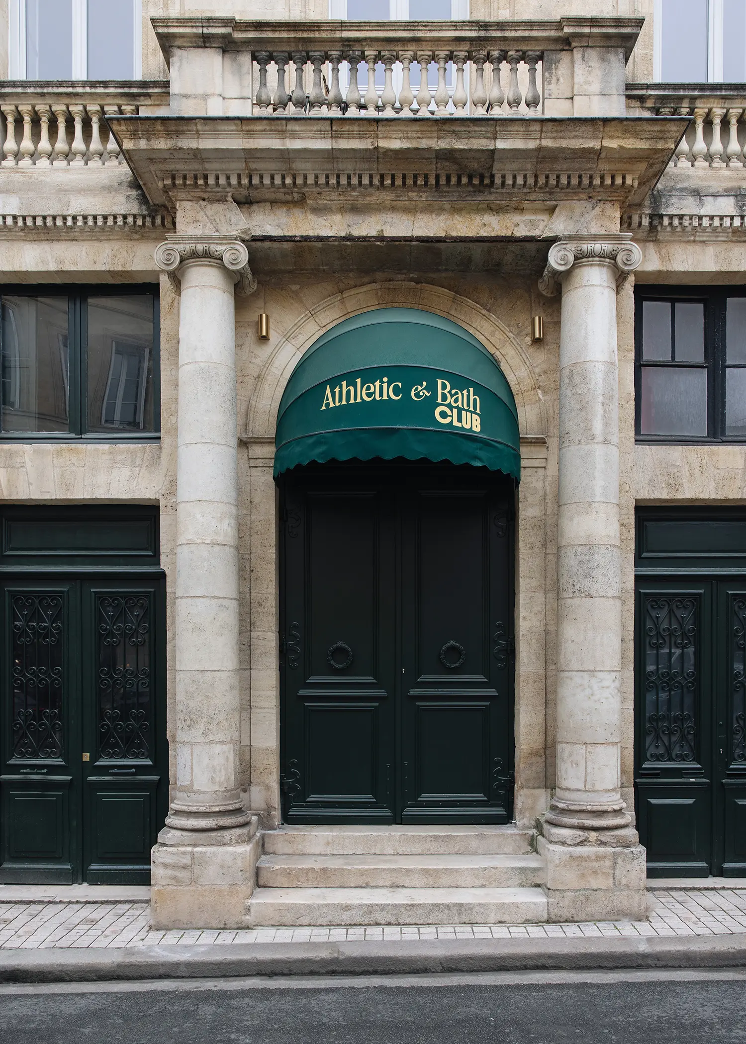 The exterior of a stone mansion in Bordeaux with a green dome awning featuring the Athletic & Bath Club logo.
