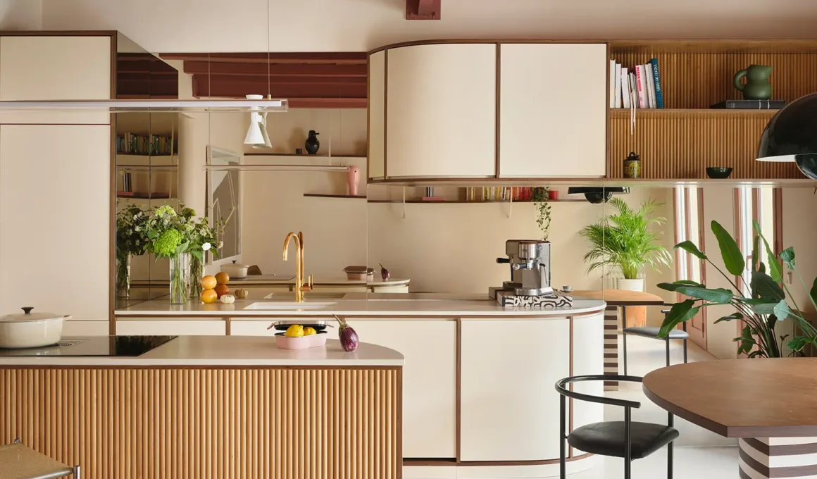 Contemporary kitchen with fluted wood island, curved cream cabinetry, and a large mirrored backsplash in a Madrid apartment.