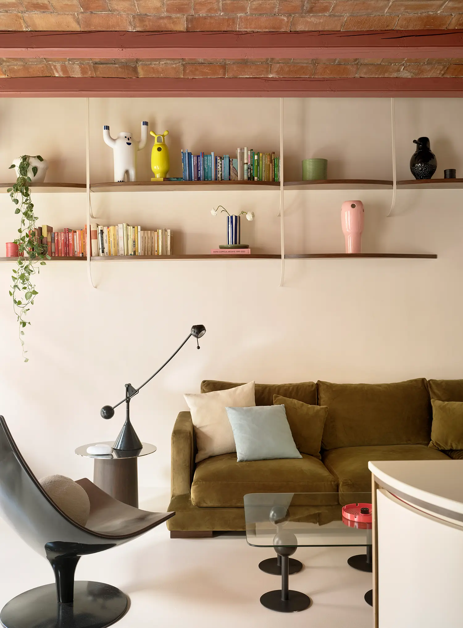 Living room with a green velvet sofa, minimalist shelving, and a traditional ceramic vaulted ceiling with pink-toned beams.