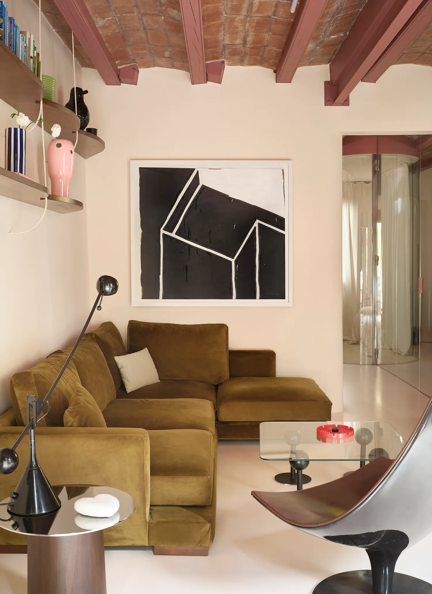 Living area featuring a curved glass partition leading to a bedroom, a green sectional sofa, and abstract black and white art.