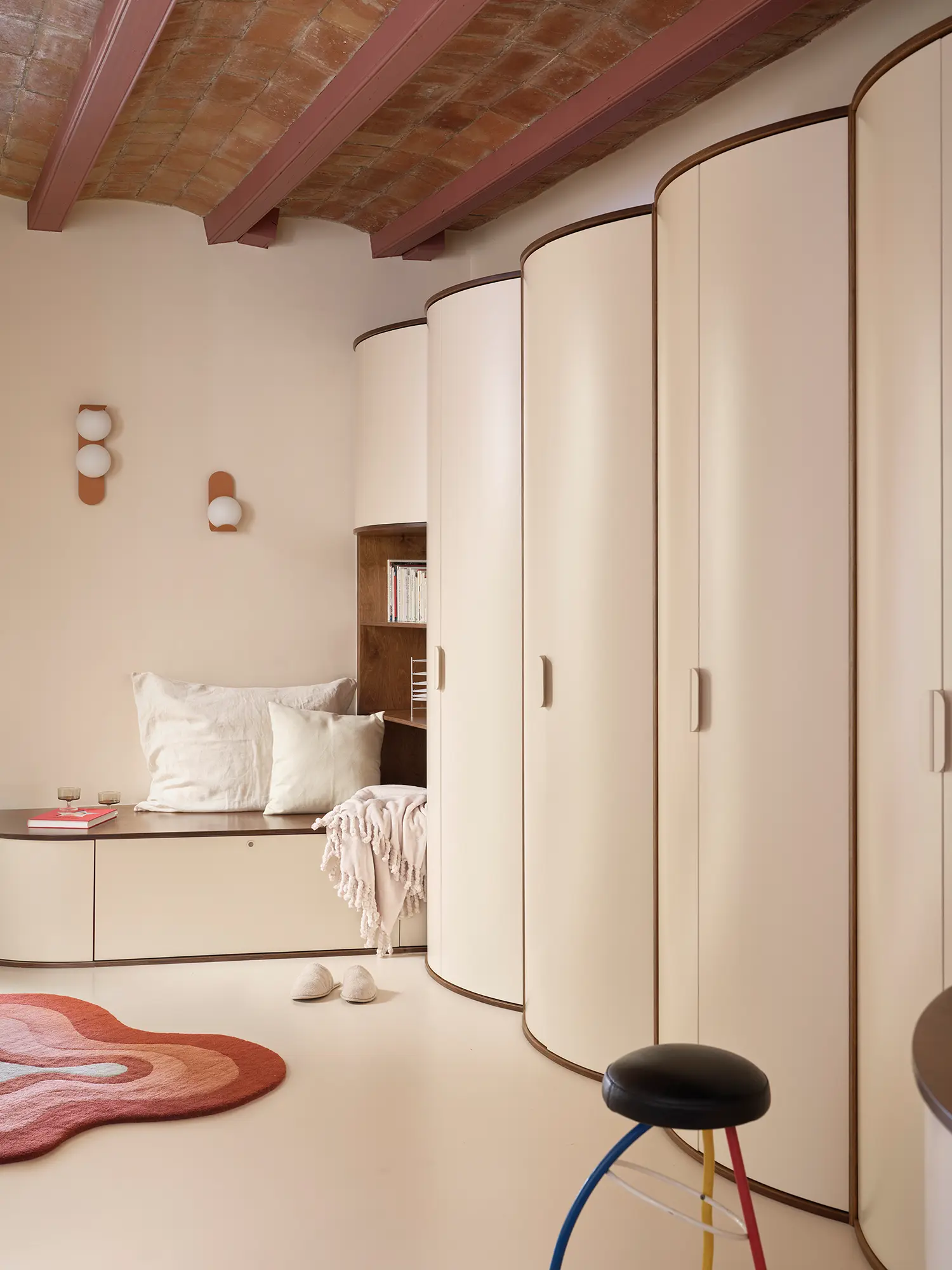 A dressing room featuring a large, curved cream wardrobe system that follows the rhythm of the vaulted ceiling.