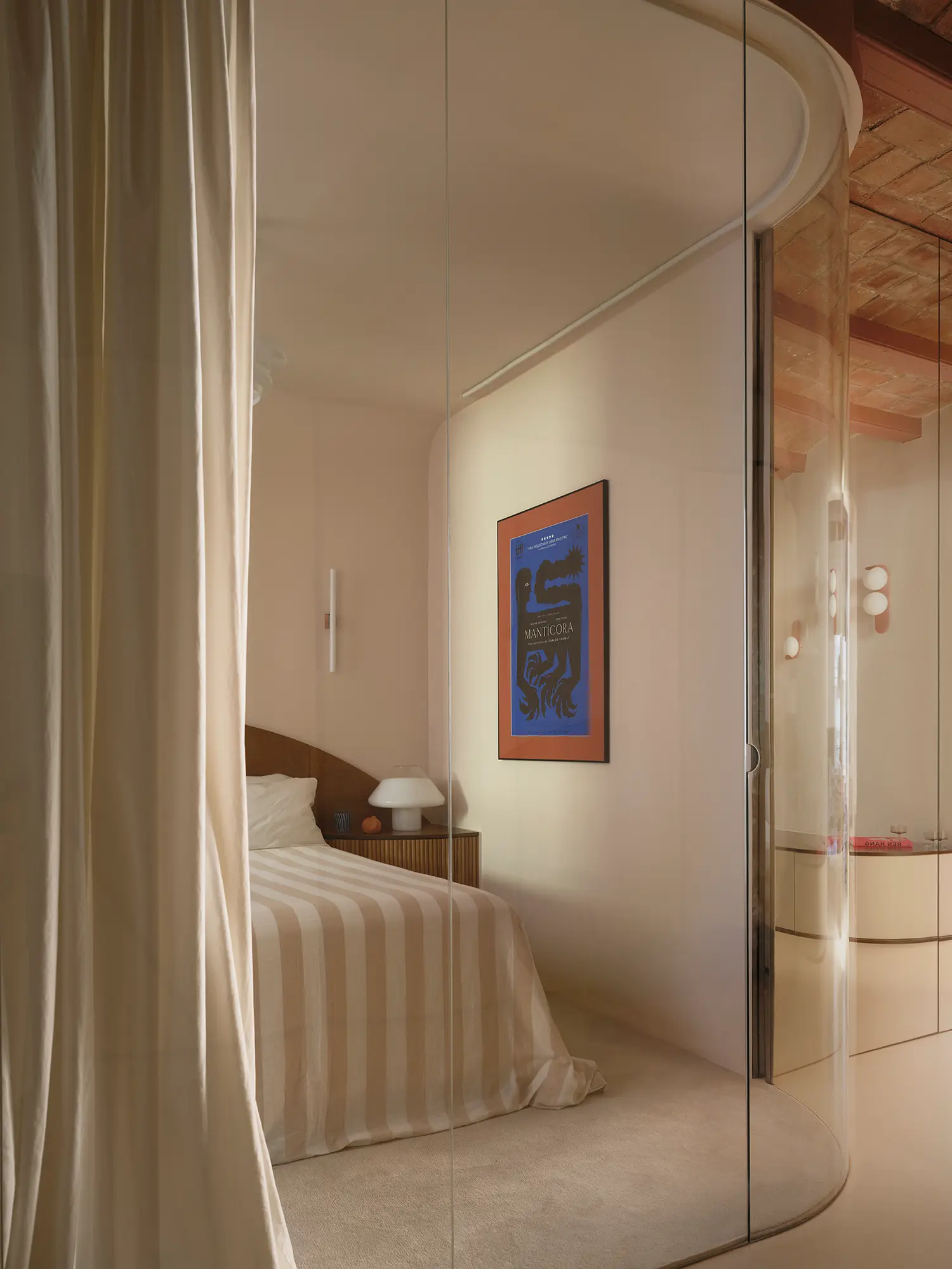 Minimalist bedroom seen through a curved glass wall with a white curtain and a traditional vaulted ceiling.