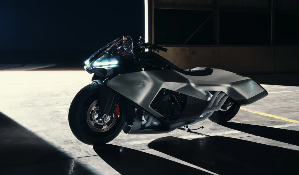 A sculptural side-profile view of the silver BMW Motorrad Vision K18 concept motorcycle in silhouette, dramatically illuminated by a narrow vertical light in a dark warehouse setting.