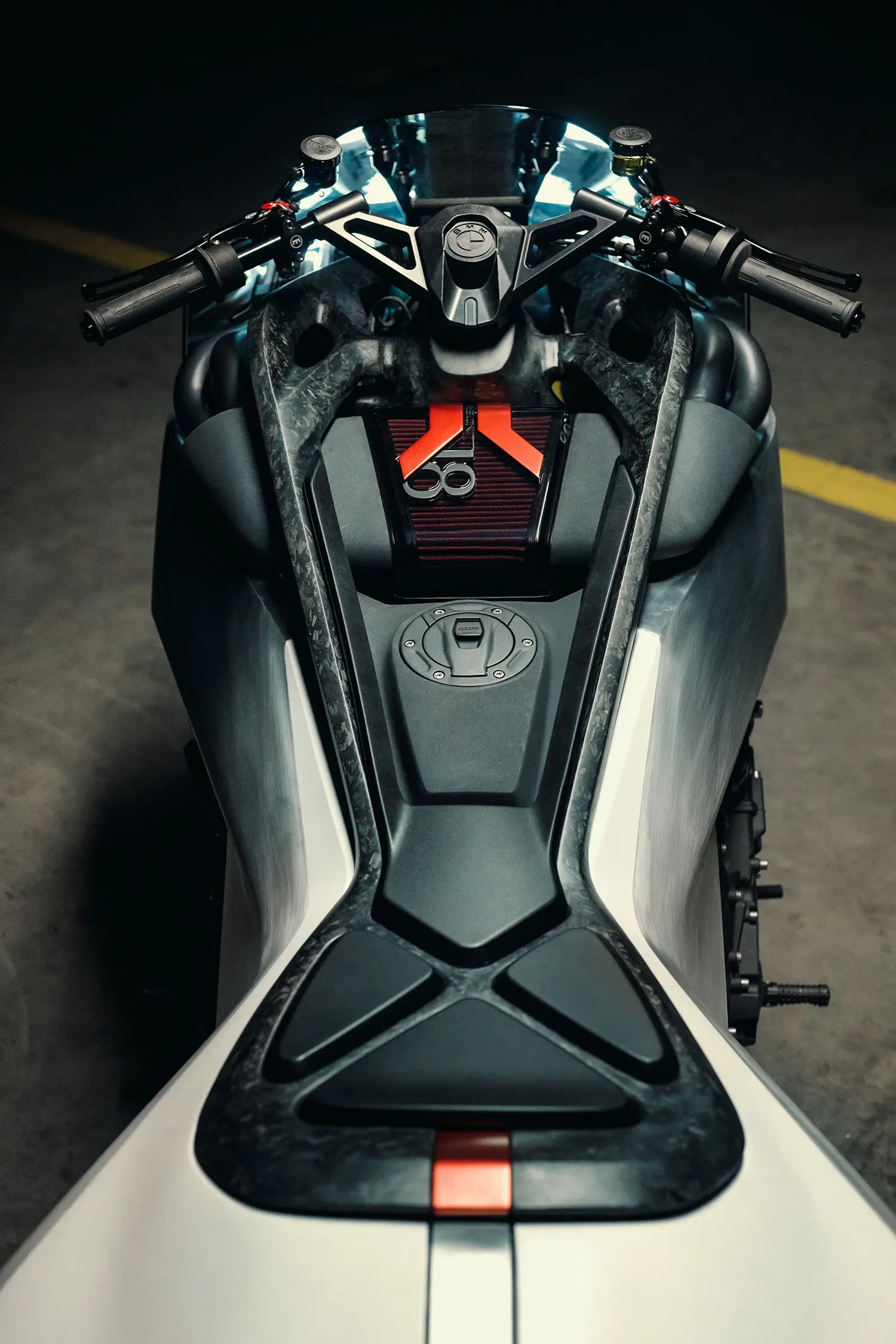 Three-quarter front view of the Vision K18, dramatic overhead lighting defining the sculpted engine and the silver body panel as it stands on a dark warehouse floor.