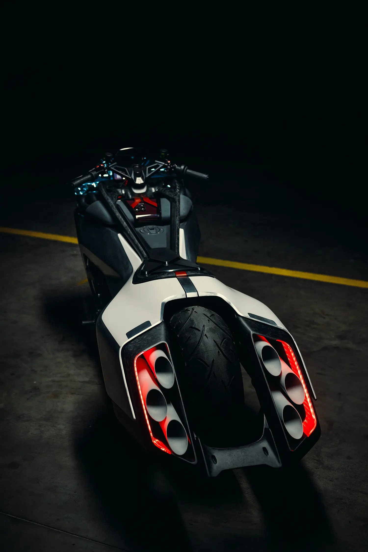 Low-angle rear view of the Vision K18, looking through a dark industrial space, focused on the wide tail section that accommodates six individual exhausts framed by glowing red LED strips.