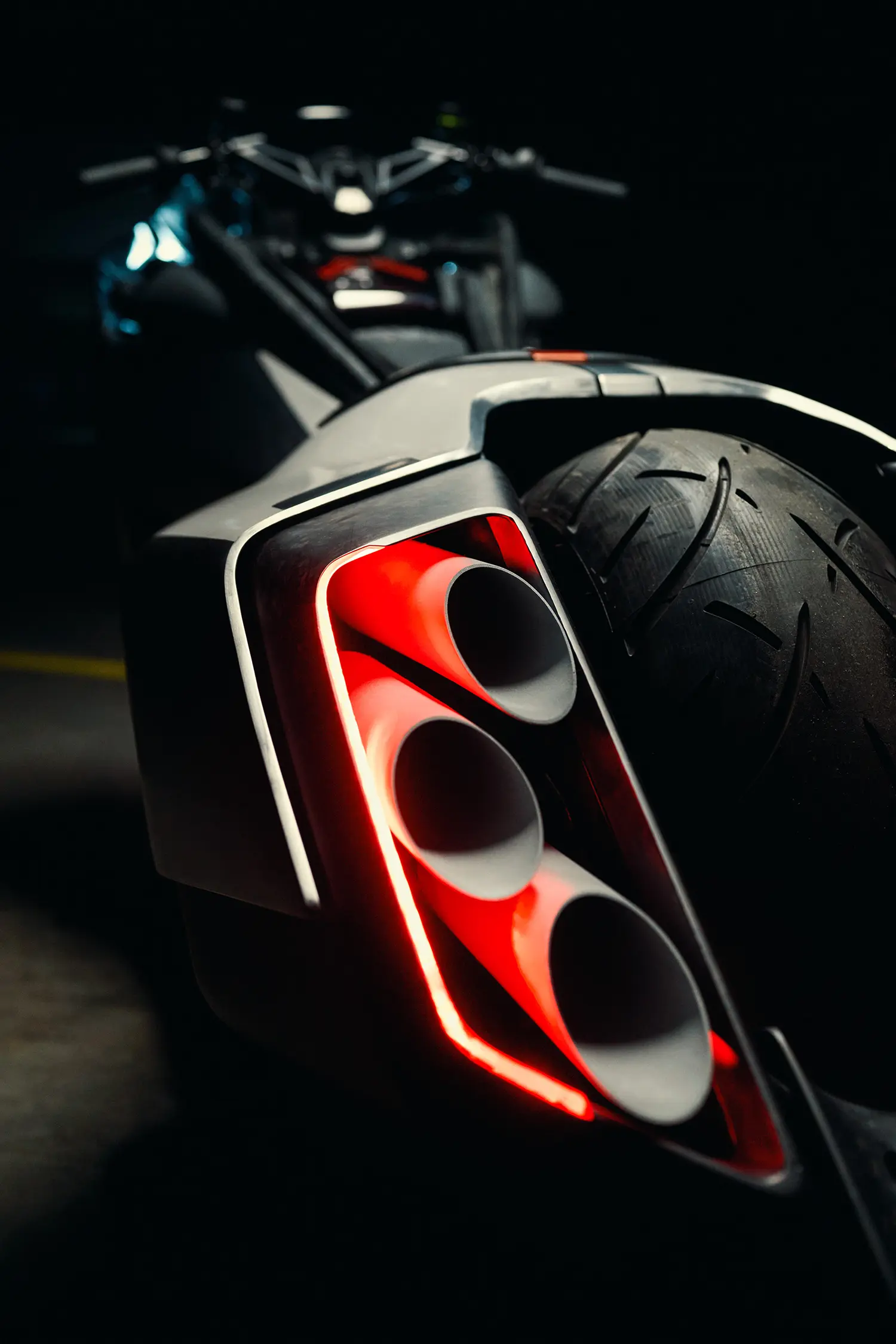 Low-angle extreme close-up of the rear tail section, showing the intricate details of the three exhaust ports on one side, each internally illuminated by a glowing red LED light.
