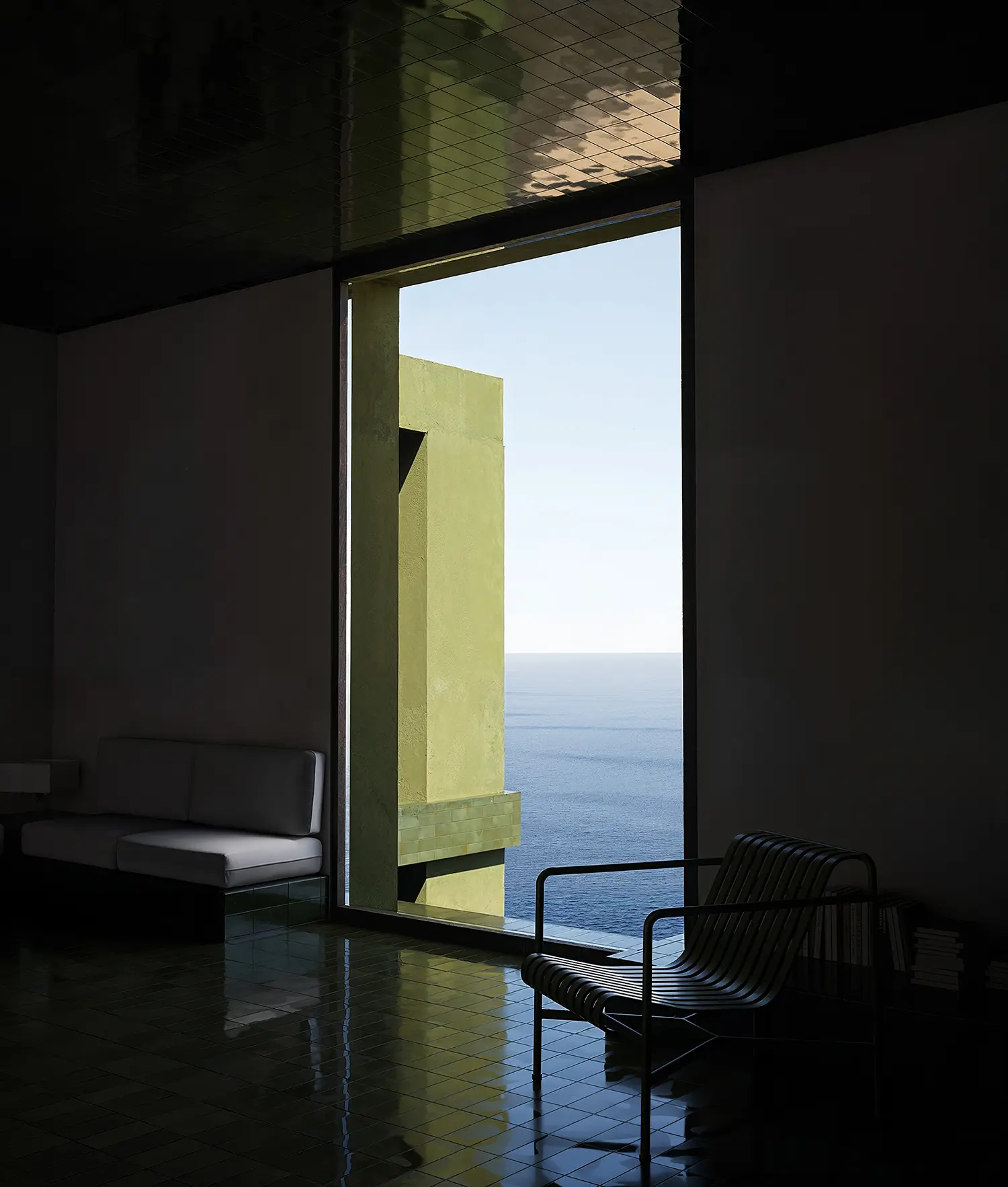 Modern living space with dark green tiled floor and large window overlooking the sea.