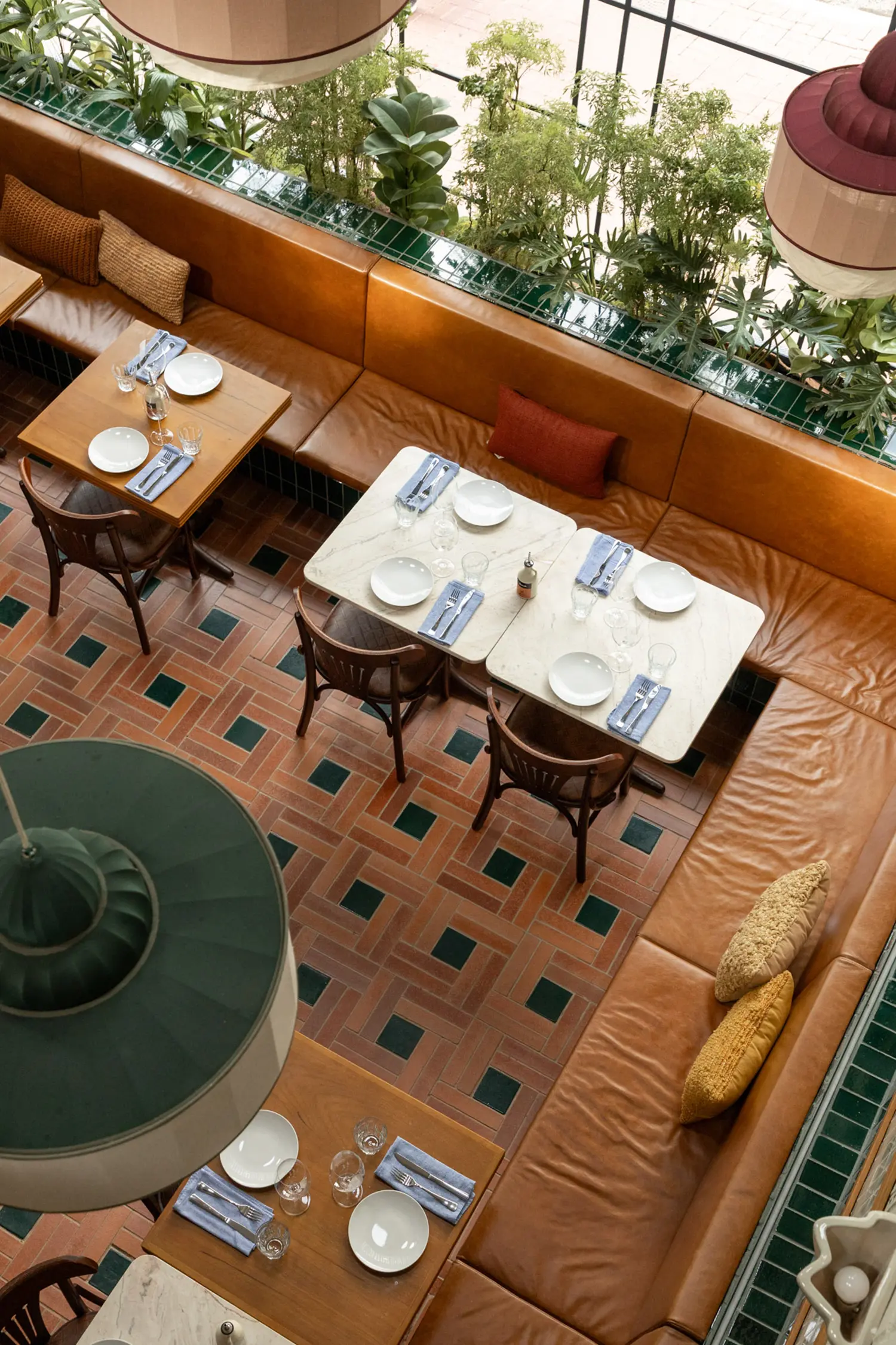 Casa Baruk Restaurant by Memola Estúdio, aerial view of banquette seating zone, terracotta and green ceramic floor tile pattern, white marble tabletops, caramel leather continuous sofa, green pendant lamp, São Paulo