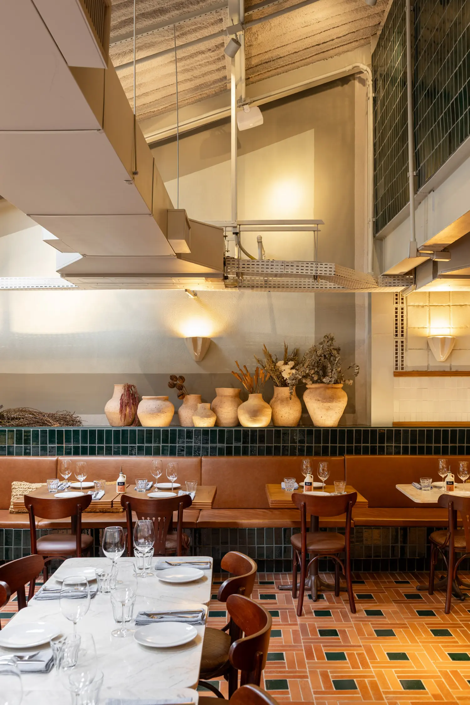 Casa Baruk Restaurant by Memola Estúdio, mezzanine dining area, shed roof skylights, exposed ductwork, shell-shaped wall sconces, terracotta ceramic amphora collection on shelf, green tile dado, São Paulo