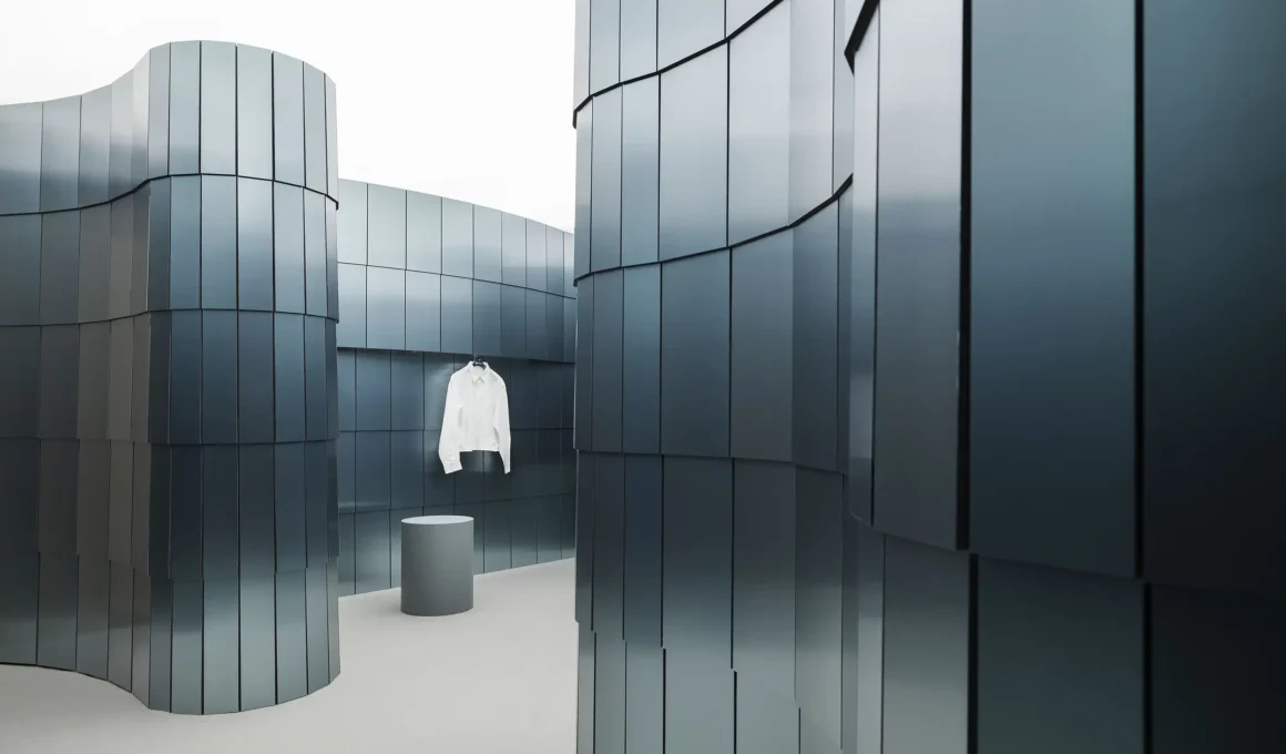 Curving walls clad in vertical matte teal metallic panels with a single white shirt hanging in the background.