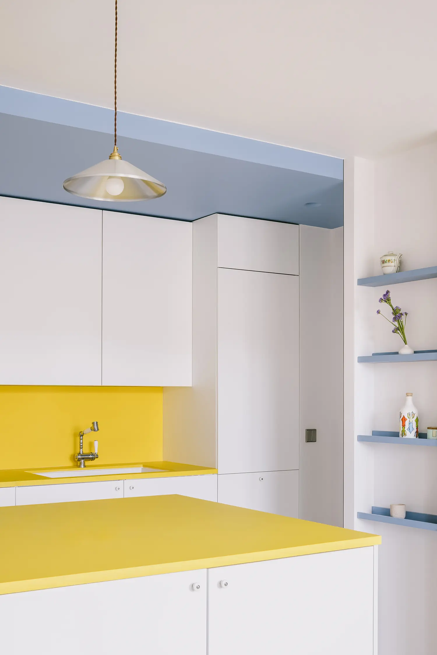 Modern white kitchen with a bright yellow countertop and backsplash under a light blue recessed ceiling.