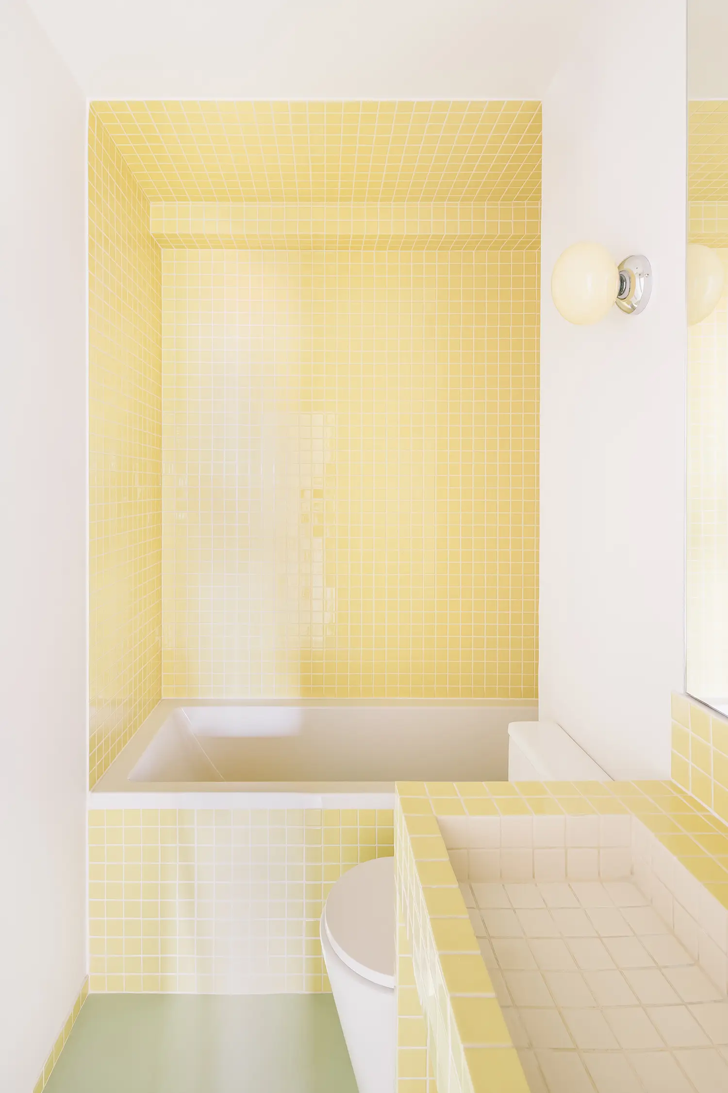 Contemporary bathroom featuring small yellow square tiles on the walls, sink, and bathtub area.