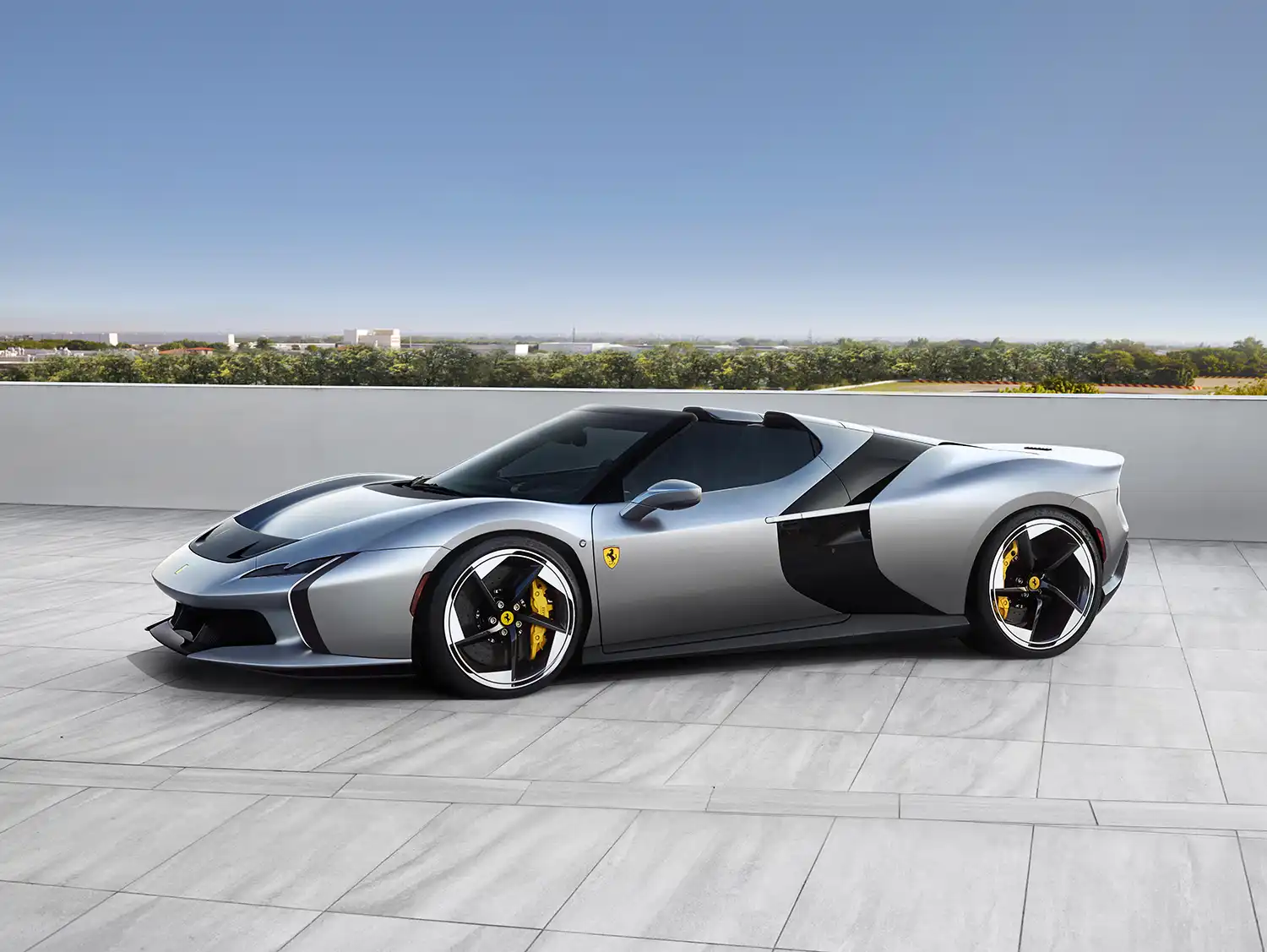 Front three-quarter view of the silver Ferrari HC25 spider showcasing its sleek profile and custom wheels against a clear blue sky.