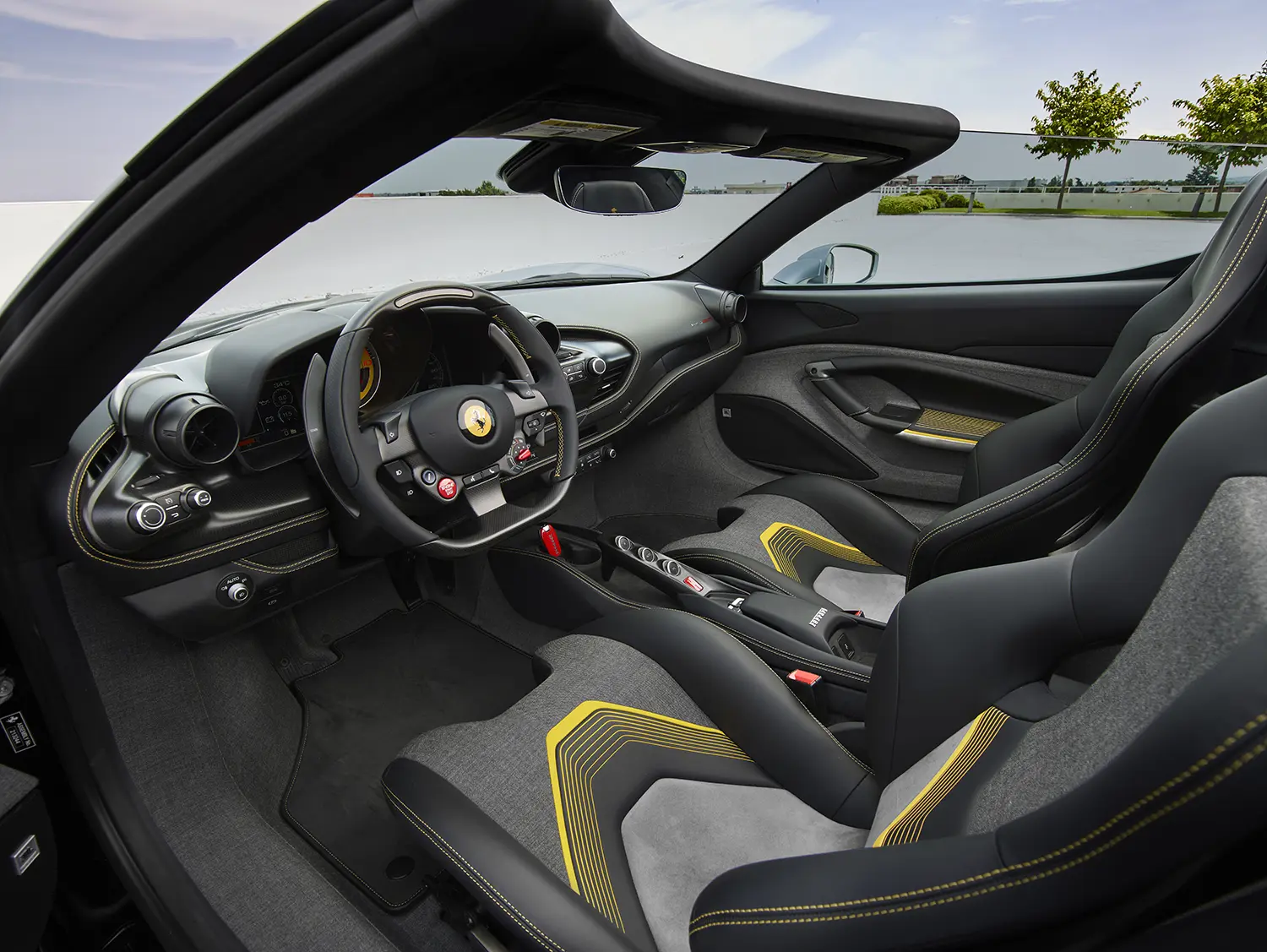 Interior cockpit view of the Ferrari HC25 from the driver side showing the steering wheel and yellow-accented bucket seats.