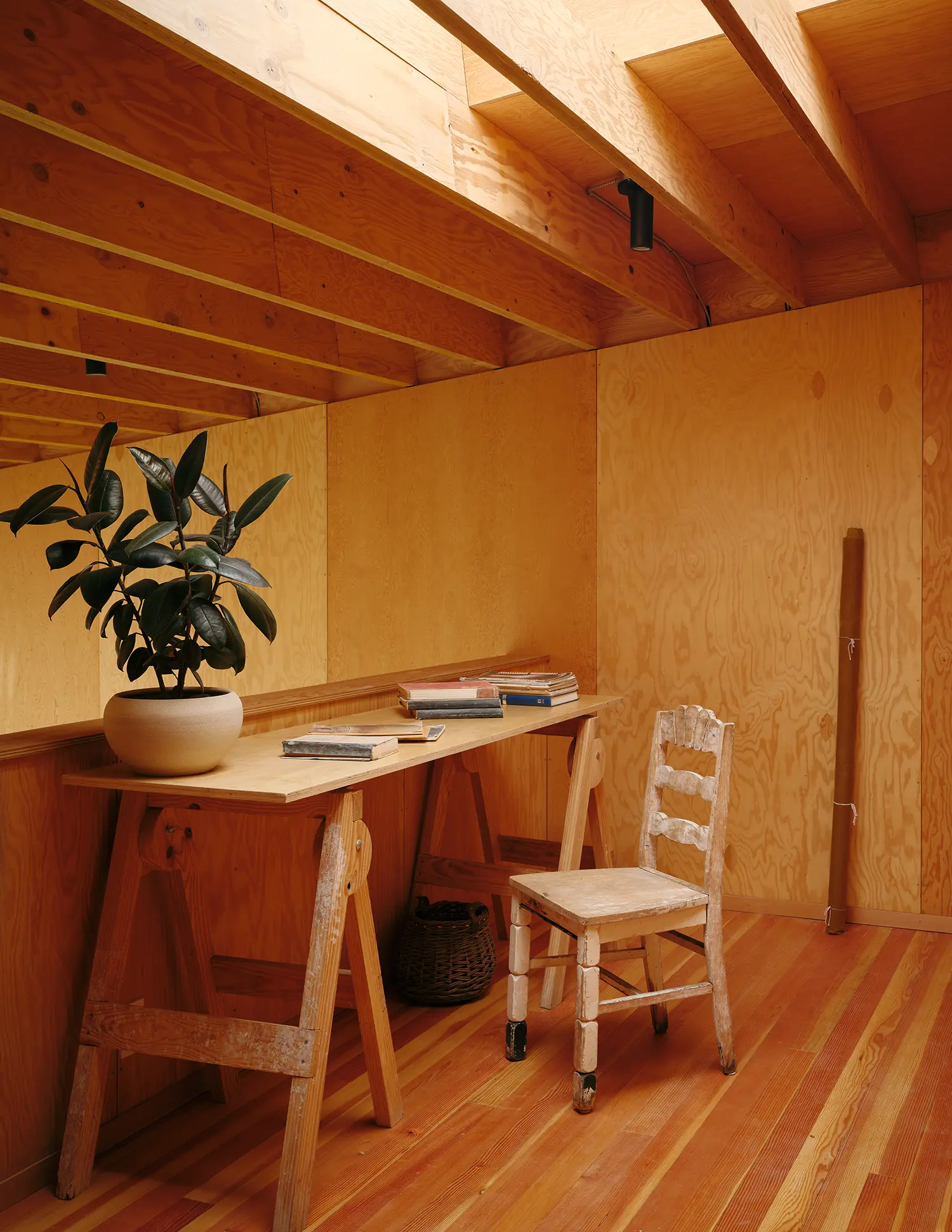 A simple wooden trestle desk and vintage chair in a plywood-lined loft space with a rubber plant.