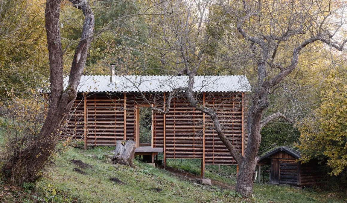 Elevated timber sauna structure with horizontal wood slat cladding on a grassy slope surrounded by autumn trees.