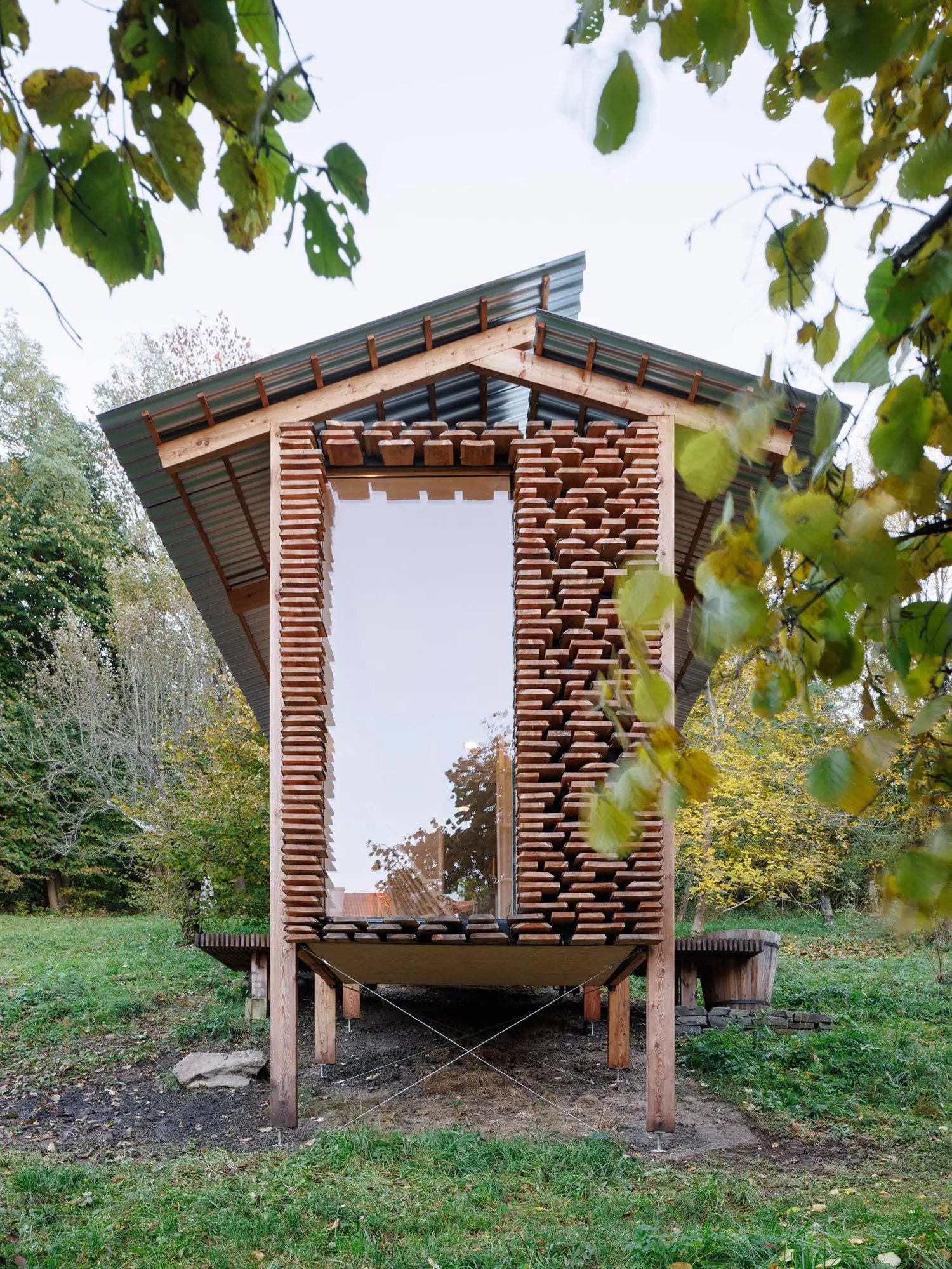 Narrow end facade of a timber building featuring a large glass window flanked by layered, stacked wooden planks.