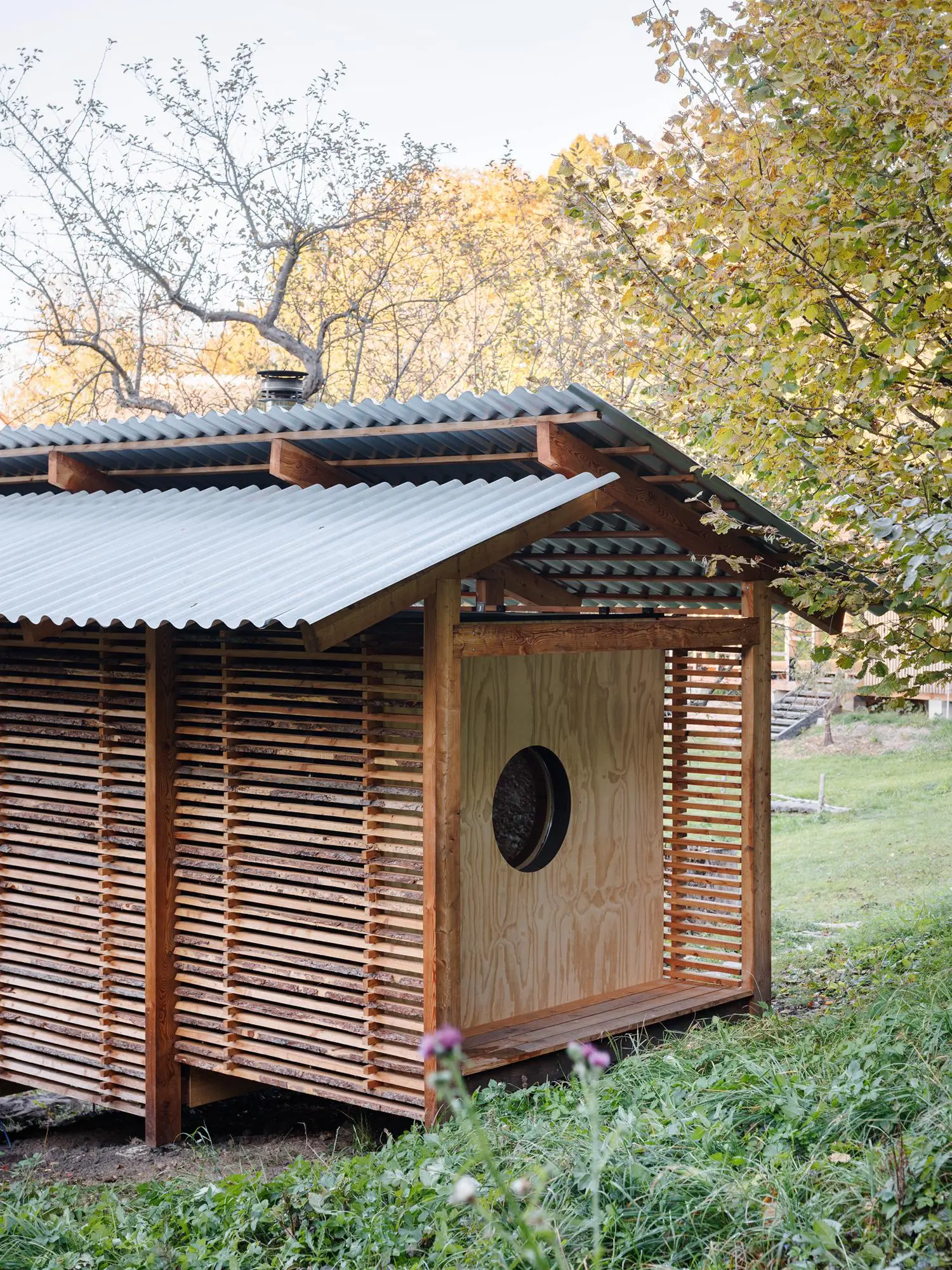 Corrugated metal roof over a timber building section featuring a light wood panel with a circular cutout window.