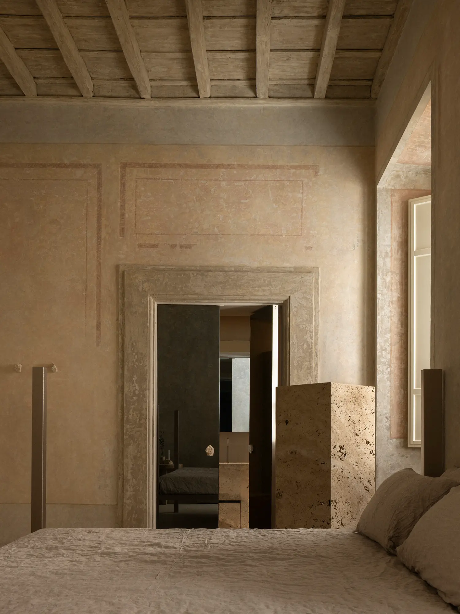 Bedroom suite at Nomos Hotel with faded frescoed walls, a travertine column, and a modern bed.