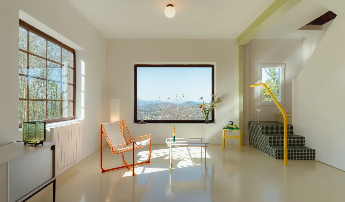 Minimalist living room in Siero with a large picture window framing the Asturian mountains, an orange wire chair, and glossy beige epoxy floors.