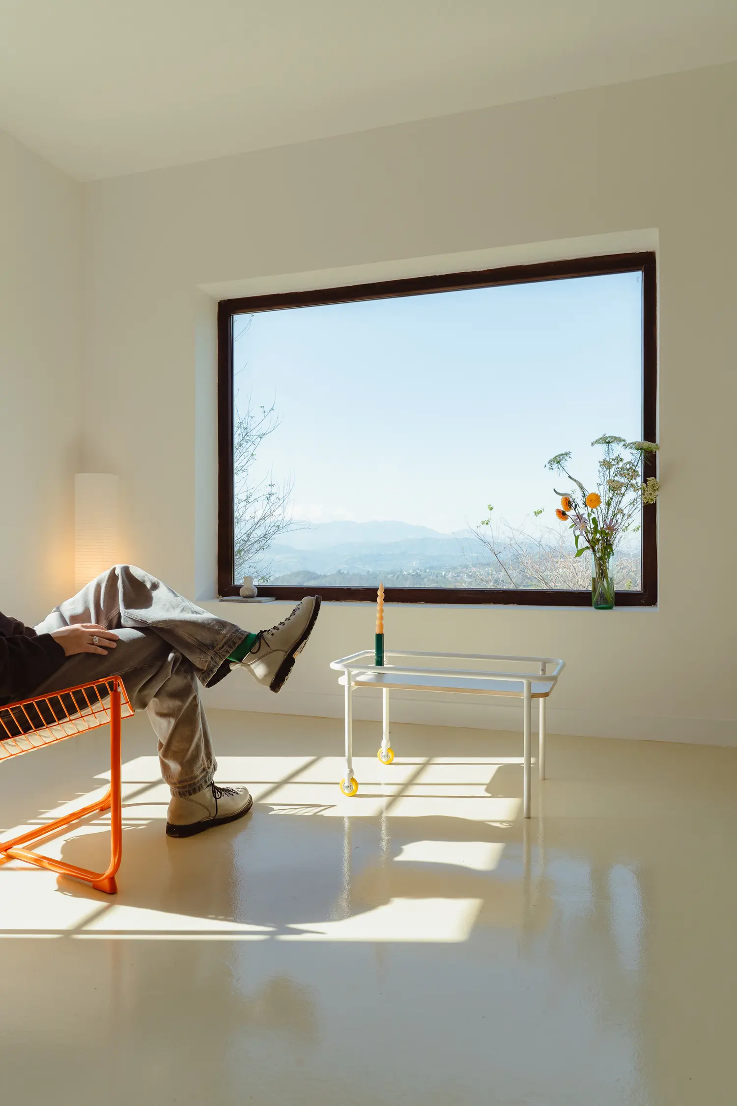 Person relaxing in an orange chair facing a large window with a panoramic view of the Spanish countryside.