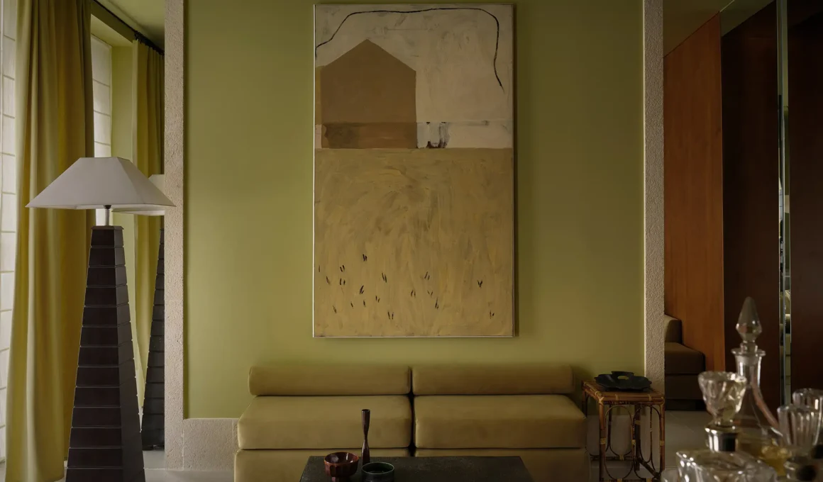 Muted olive-green living room featuring a low velvet sofa, a minimalist black coffee table, and a large abstract canvas painting between two floor-to-ceiling mirror panels.