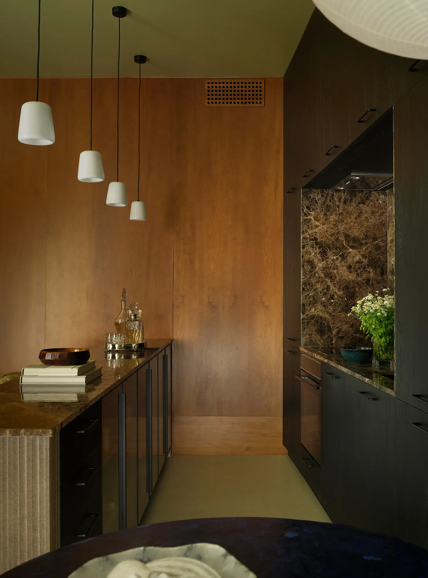 Narrow kitchen corridor showing a dark wood floor-to-ceiling cabinet system with an integrated Emperador marble splashback next to a warm oak volume.