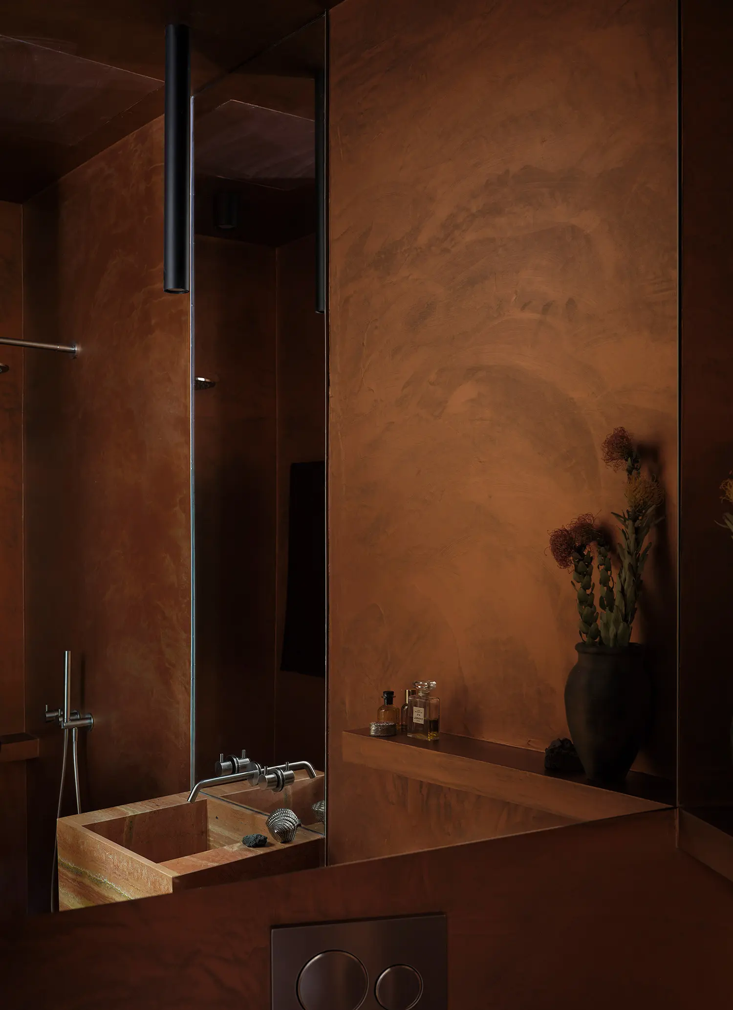 Introspective bathroom interior featuring earth-toned microcement walls, a red travertine marble vanity basin, and full-height mirrors.