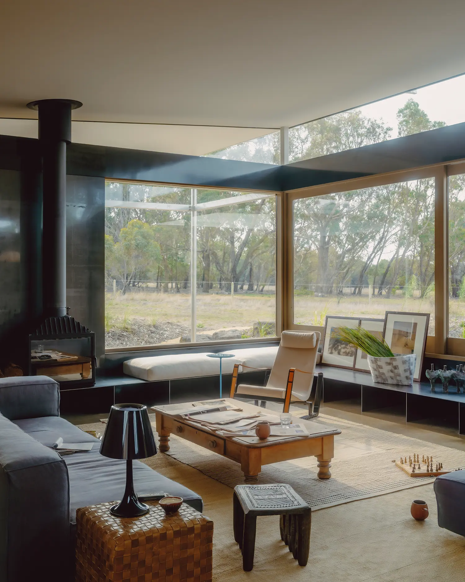 Interior living room of Ironbark House with a central steel hearth, wooden coffee table, and large windows overlooking the bushland.