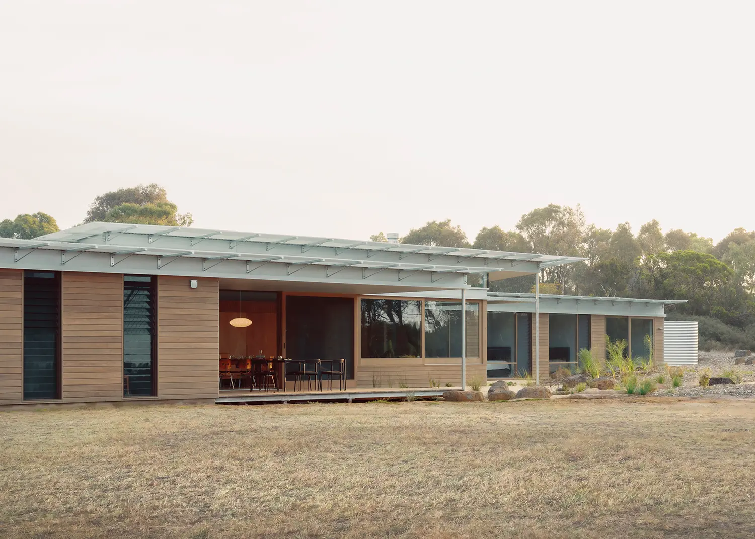 Twilight view of the additive modular layout of Ironbark House with illuminated interiors and timber facades.