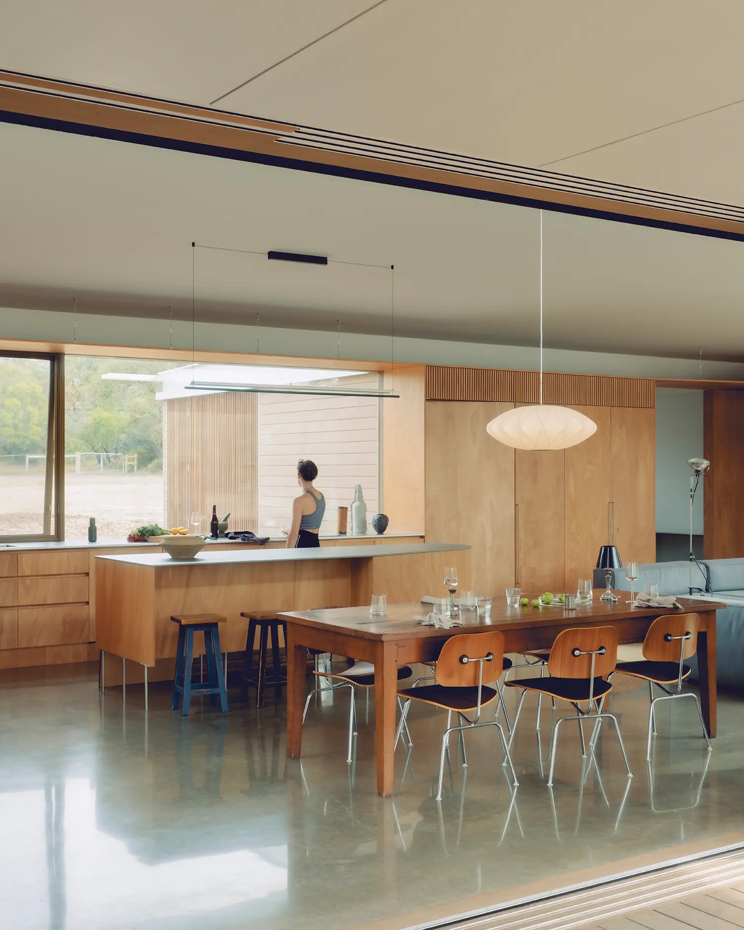 Open-plan kitchen and dining area with plywood joinery, a large island, and a Nelson Bubble Lamp.
