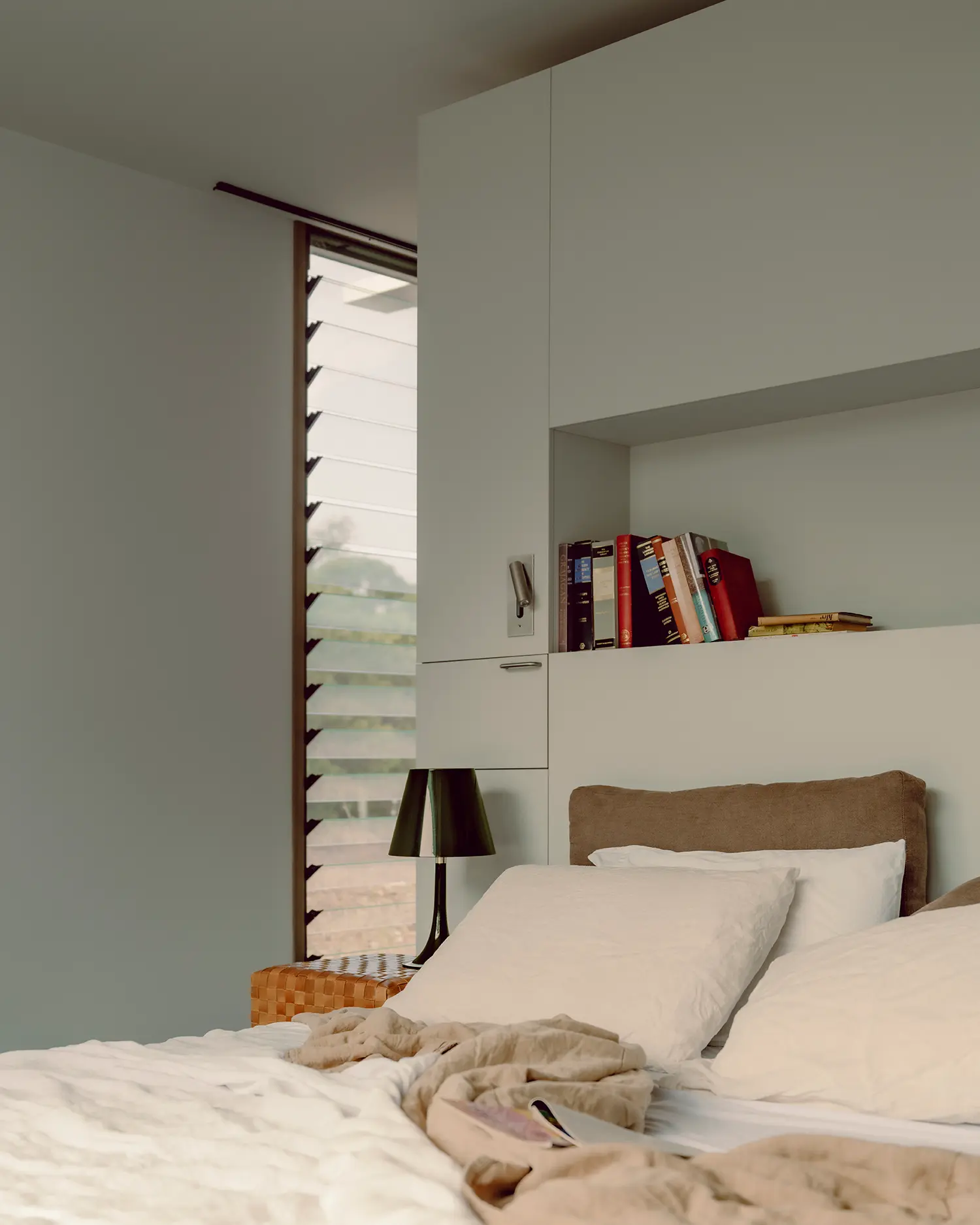 Bedroom interior featuring built-in white cabinetry, a recessed bookshelf, and louvred windows for ventilation.