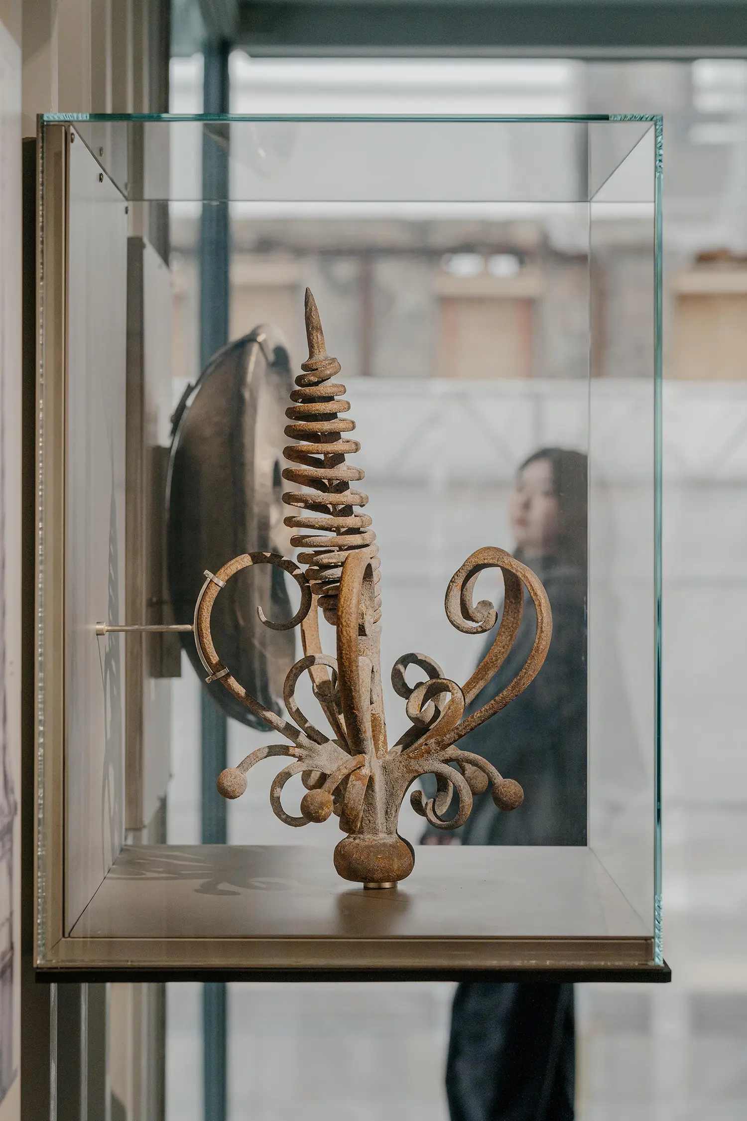A rusted, ornate metal finial displayed in a glass case within the shipping container gallery.