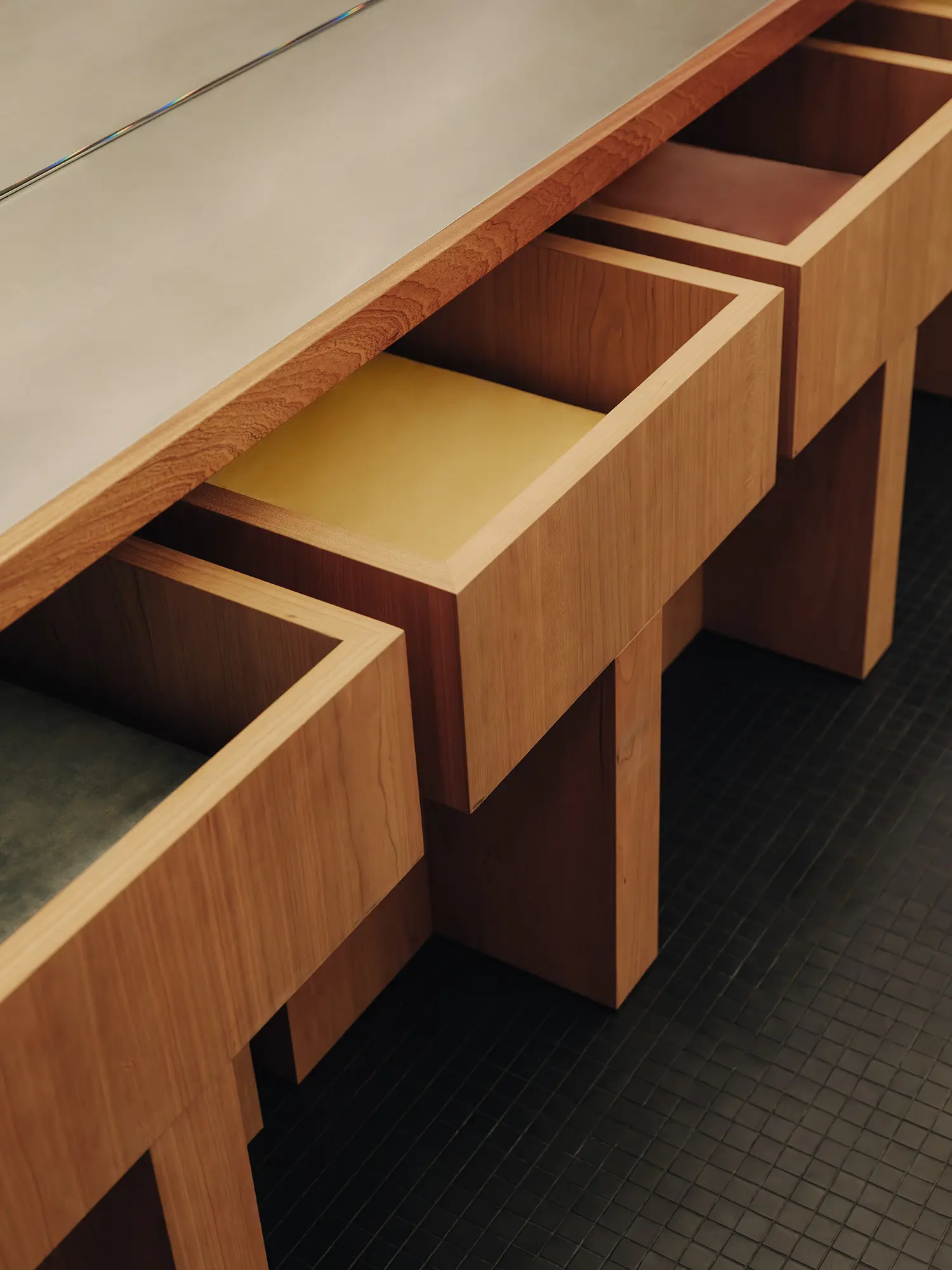 Close-up detail of custom wooden bench seats with colored leather cushions nested under a concrete countertop.