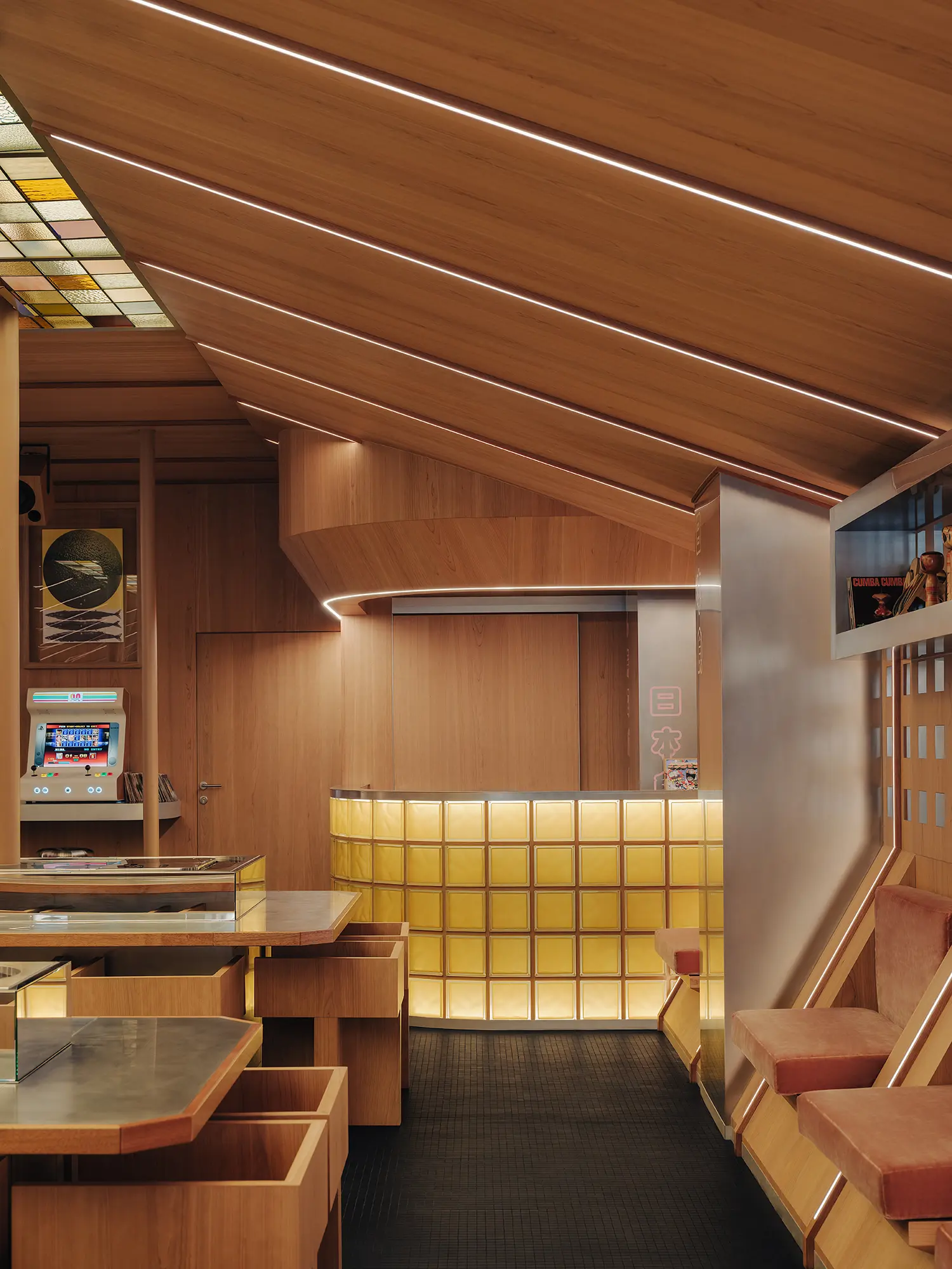 A view toward the back of Matsuri Marseille featuring a glowing yellow glass block counter, wooden wall panels, integrated seating, and a vintage arcade machine.