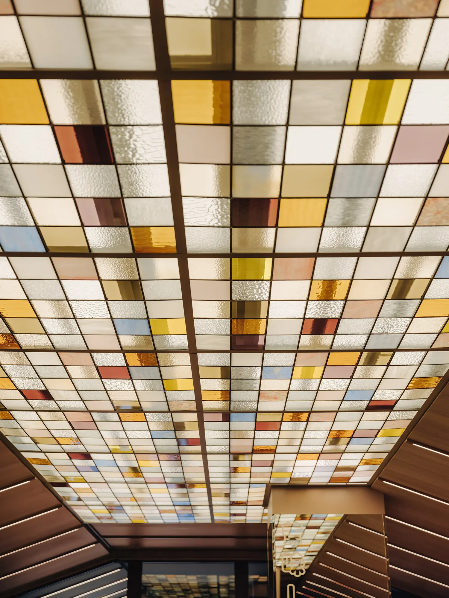 A vertical view looking straight up at a large grid of pastel-toned stained glass ceiling panels.