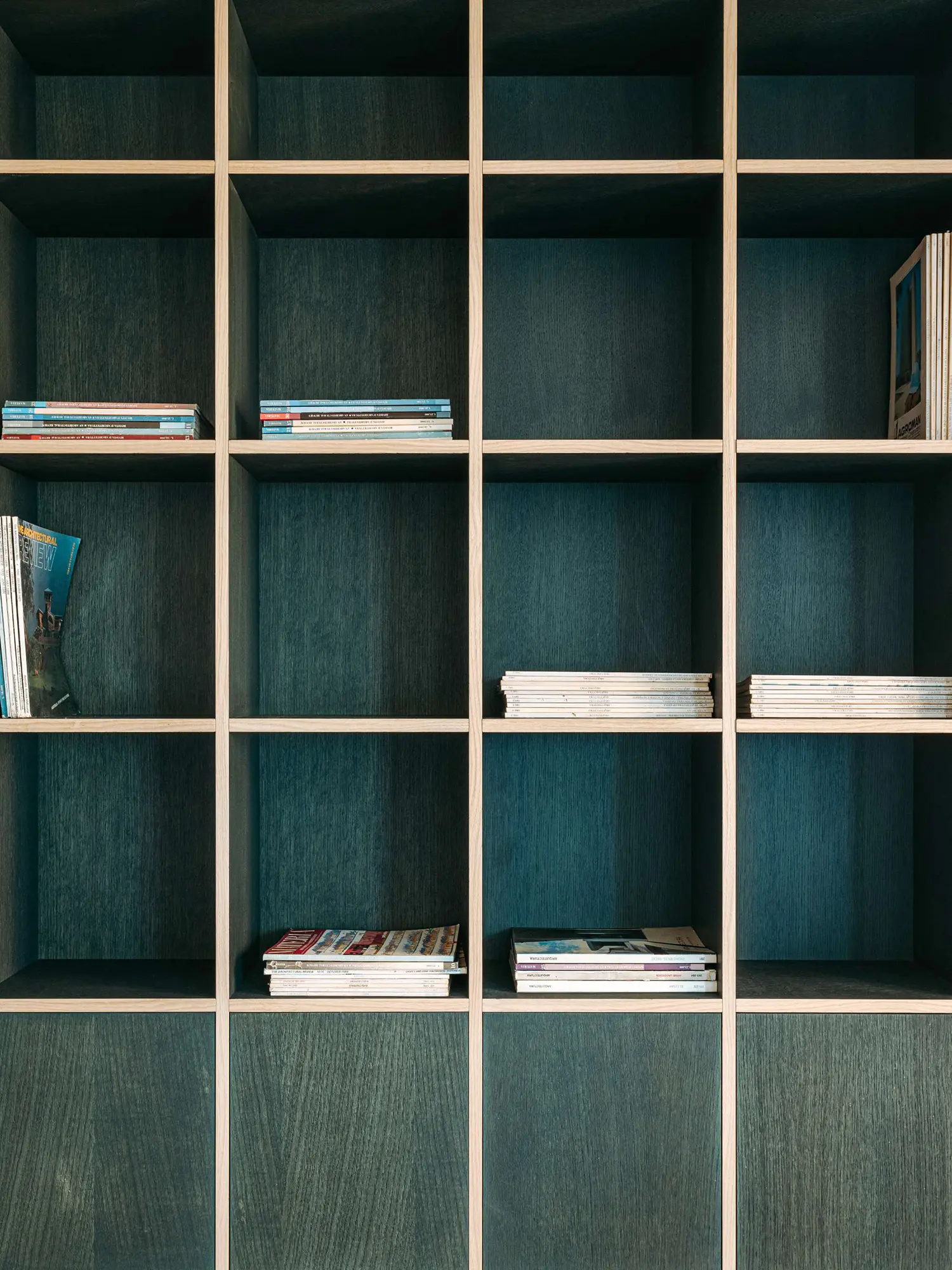 Close-up of open oak shelving grid with dark green wood grain interiors holding architectural magazines.