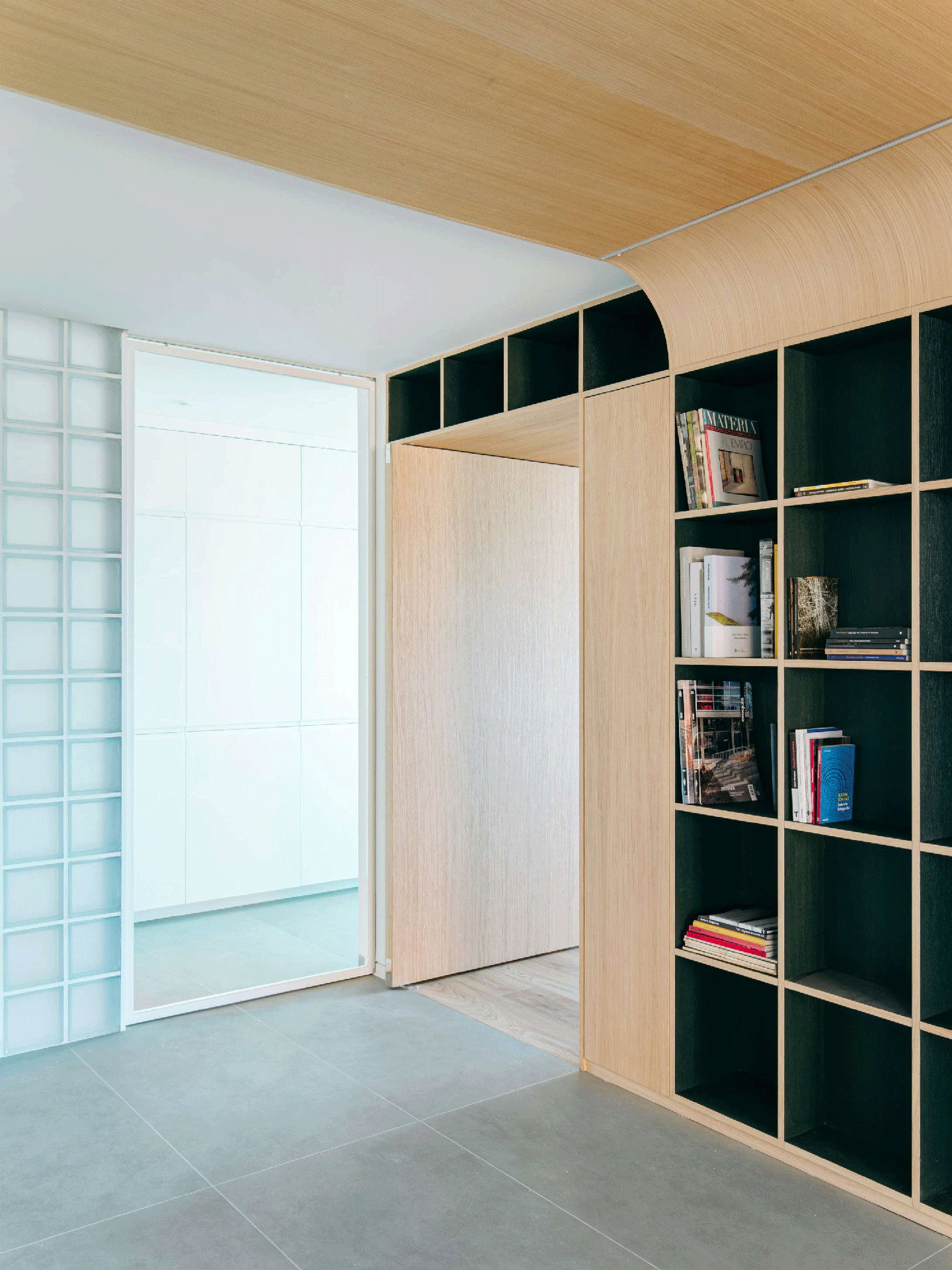 Angled view of a custom curved oak ceiling panel and built-in shelving next to a glass block wall.