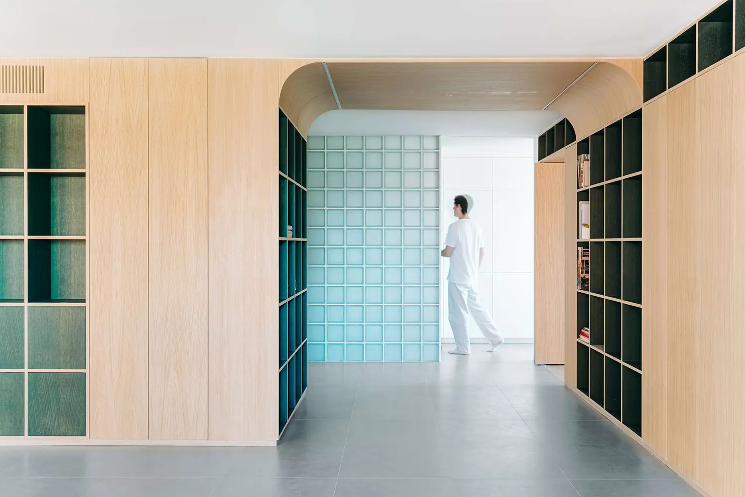 Symmetrical view of a central oak archway framing a translucent glass-block wall partition in a modern apartment.