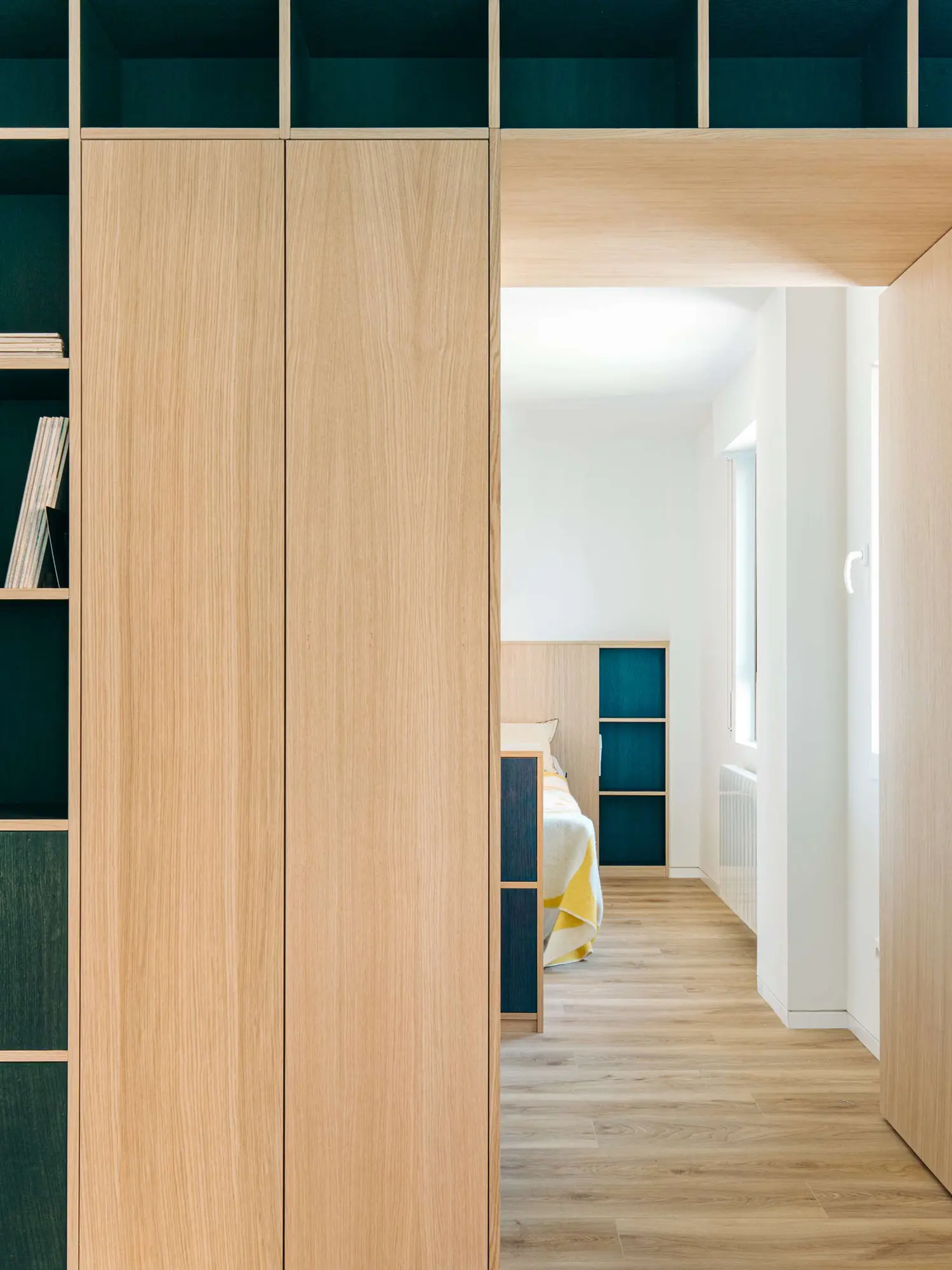 Open oak doorway looking into a minimalist bedroom with warm wood flooring and a custom headboard.