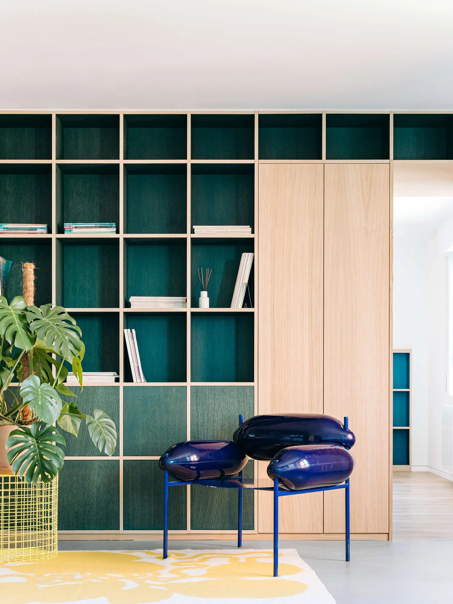 Sculptural glossy blue lounge chair in front of a custom oak and deep green gridded storage wall.