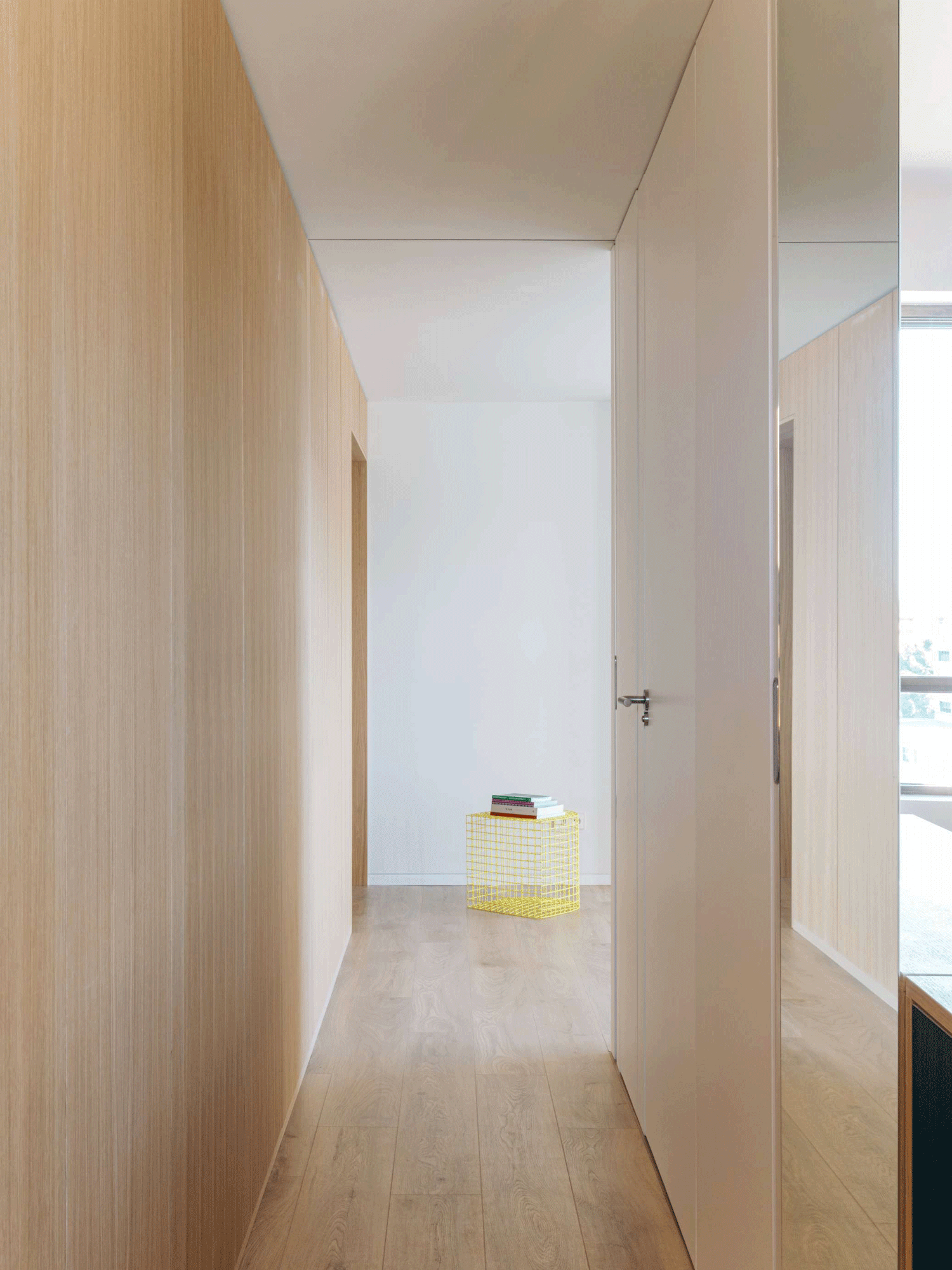 Minimalist corridor lined with full-height oak paneling on one side and glossy white doors on the other.