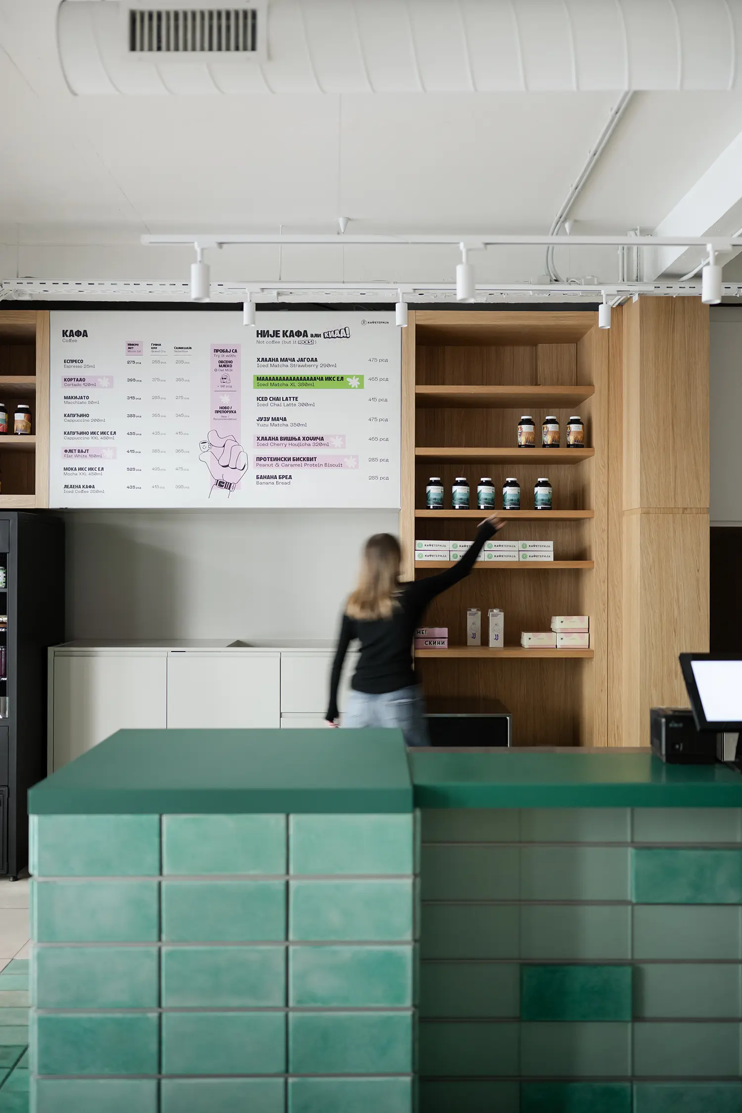 Close-up of a green tiled coffee bar and wooden shelving with a menu board above.