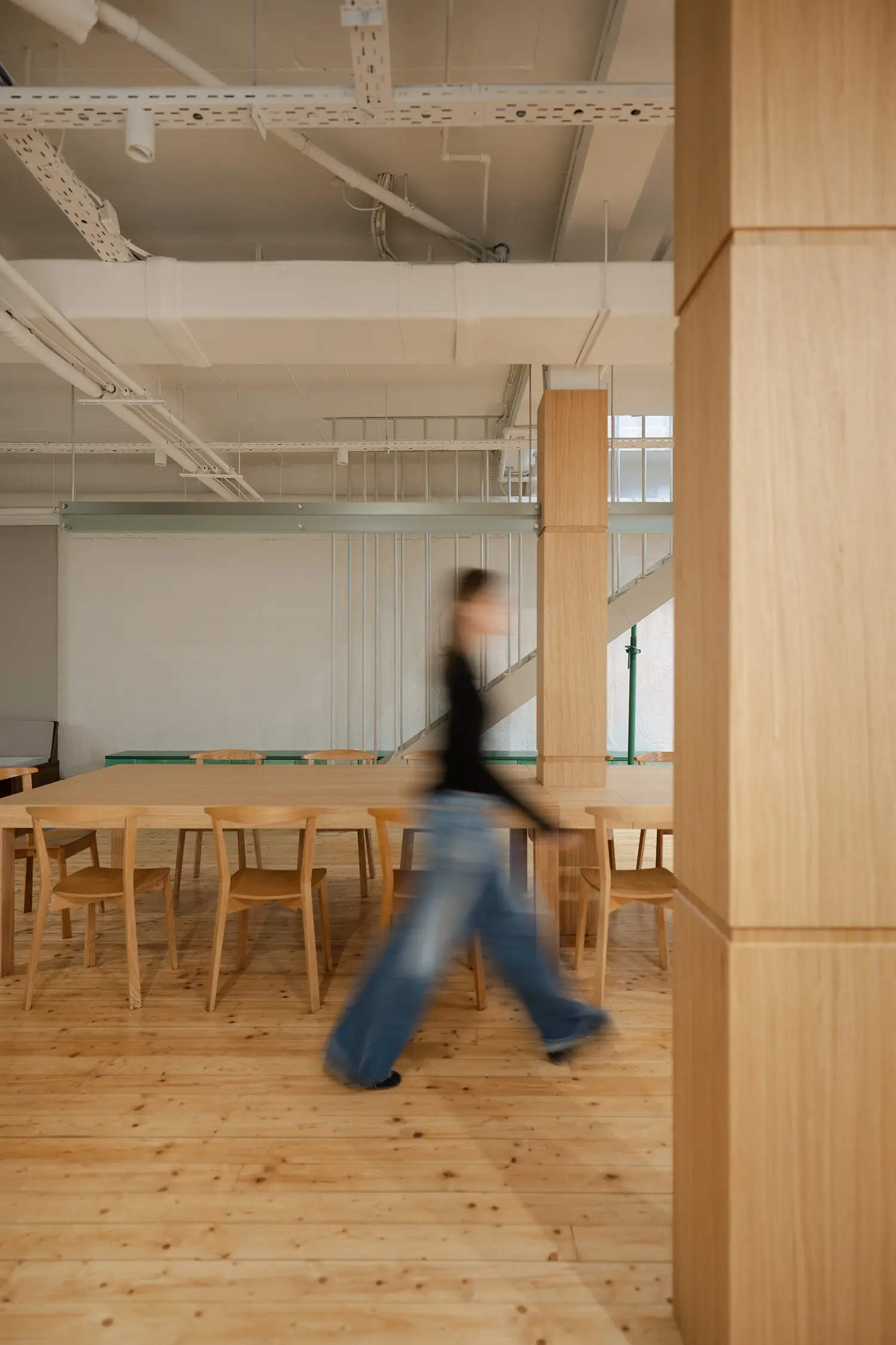 A long communal wood table with matching chairs under an industrial white ceiling.