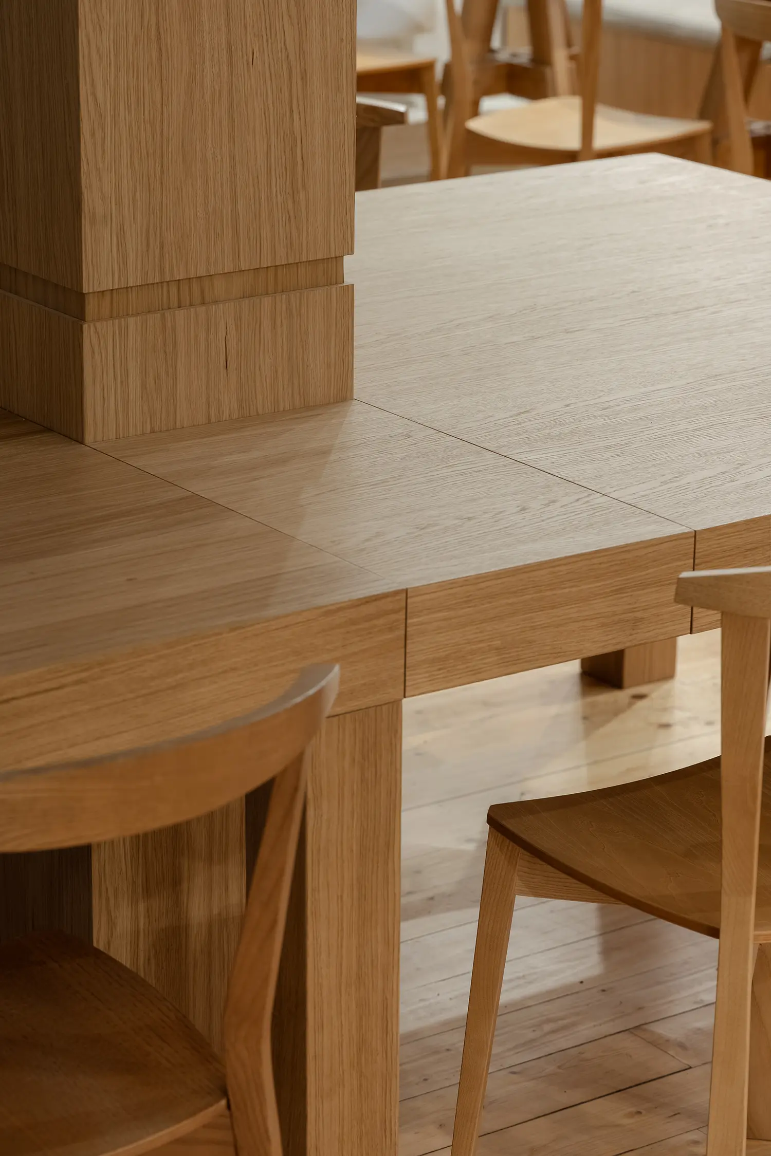 Detail shot of a smooth oak communal table built around a central wooden column base.