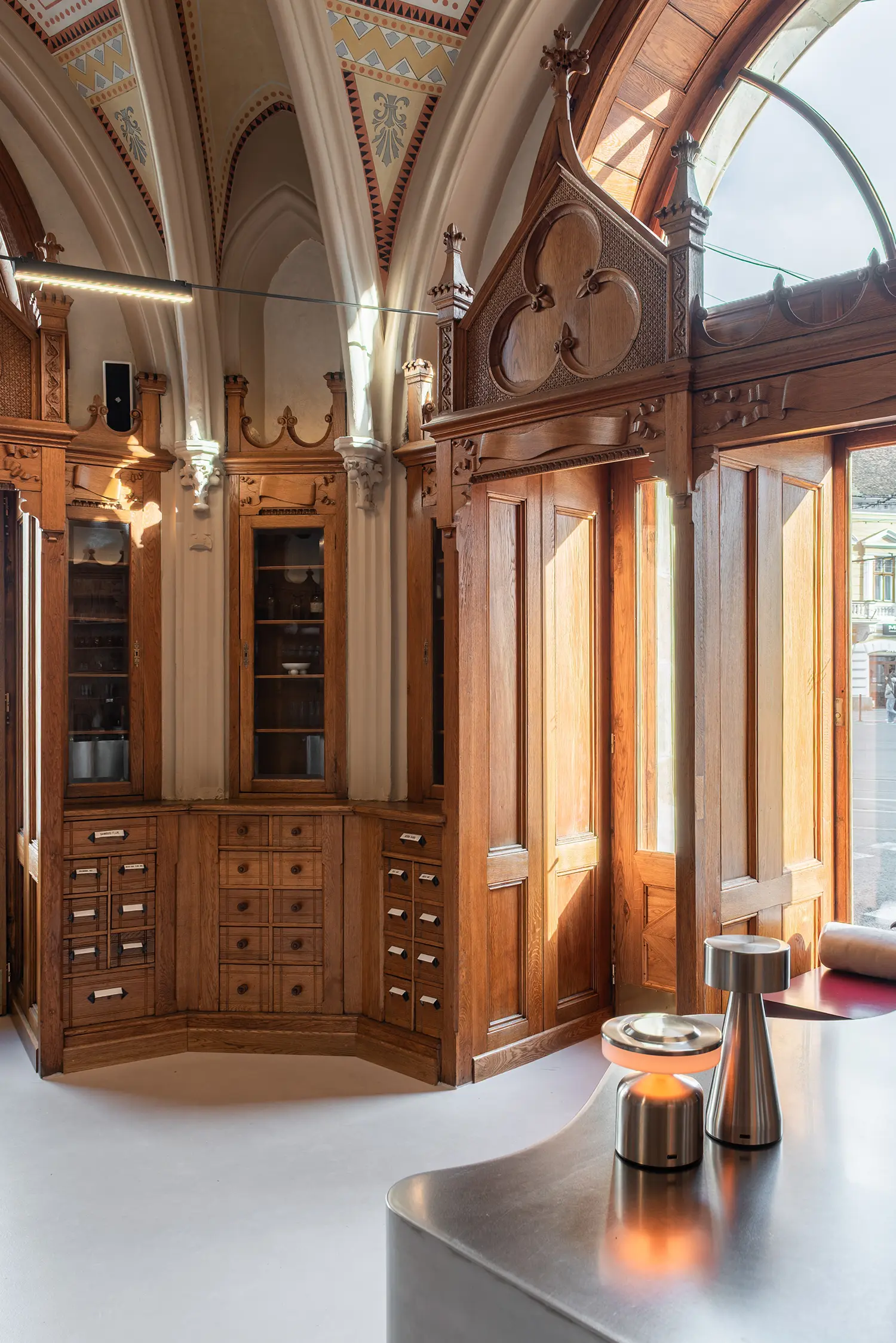 Detailed view of restored wooden pharmacy drawers and cabinets illuminated by natural light from a window.